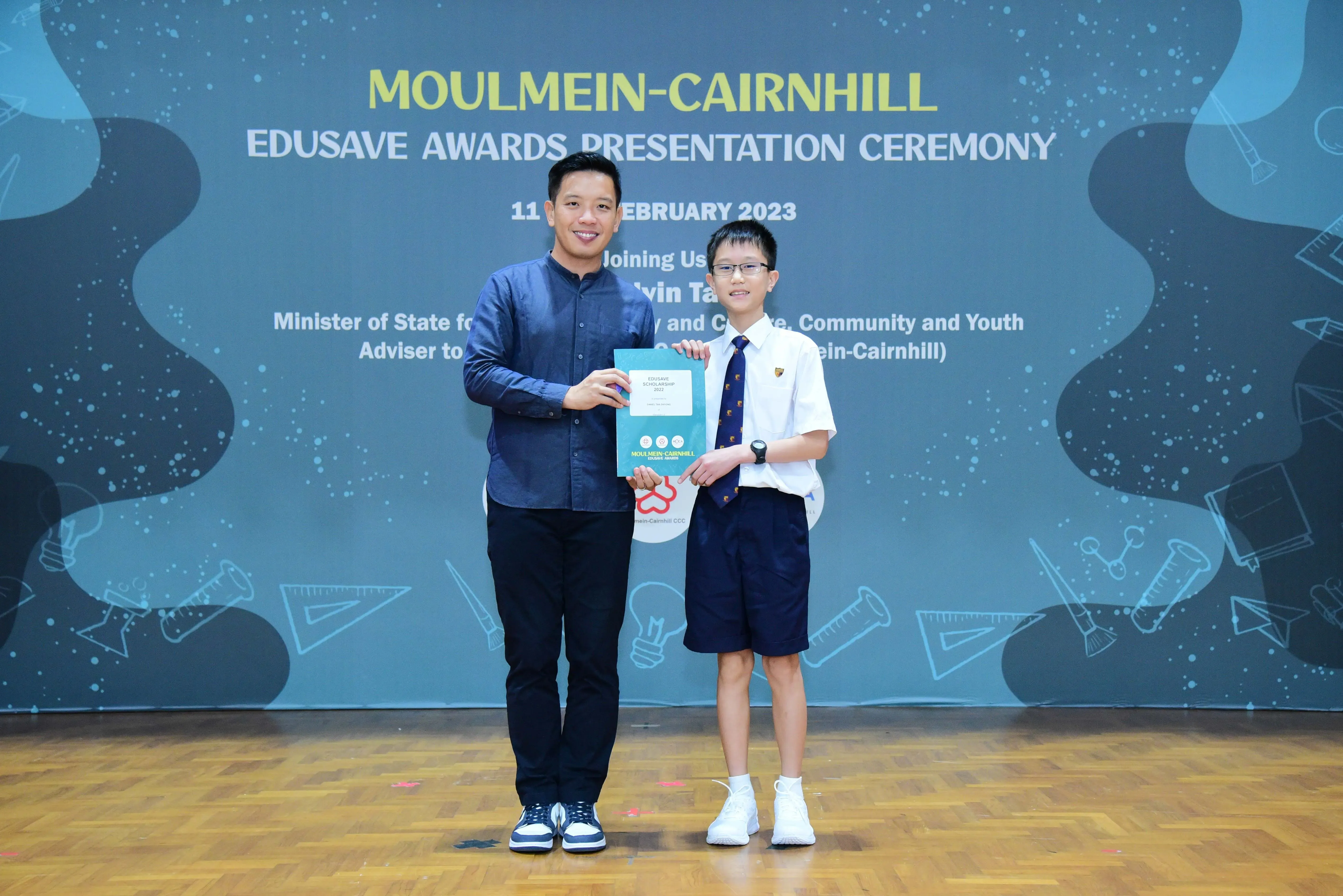 An adult and a young student hold an award at the Moulmein-Cairnhill Edusave Awards Presentation Ceremony 2023.