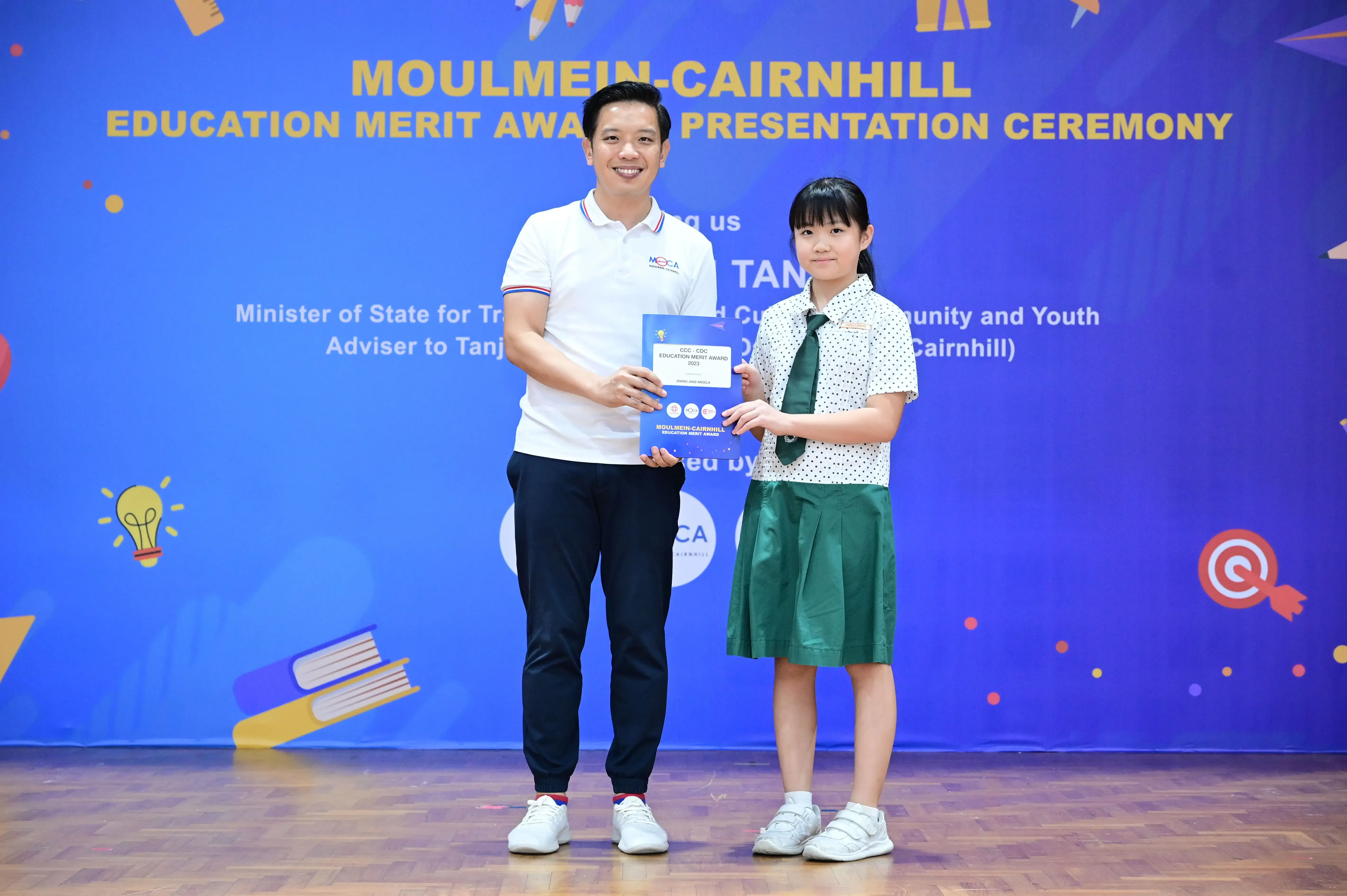 A man and a young girl in school uniform hold an award certificate at the Moulmein-Cairnhill Education Merit Award ceremony.
