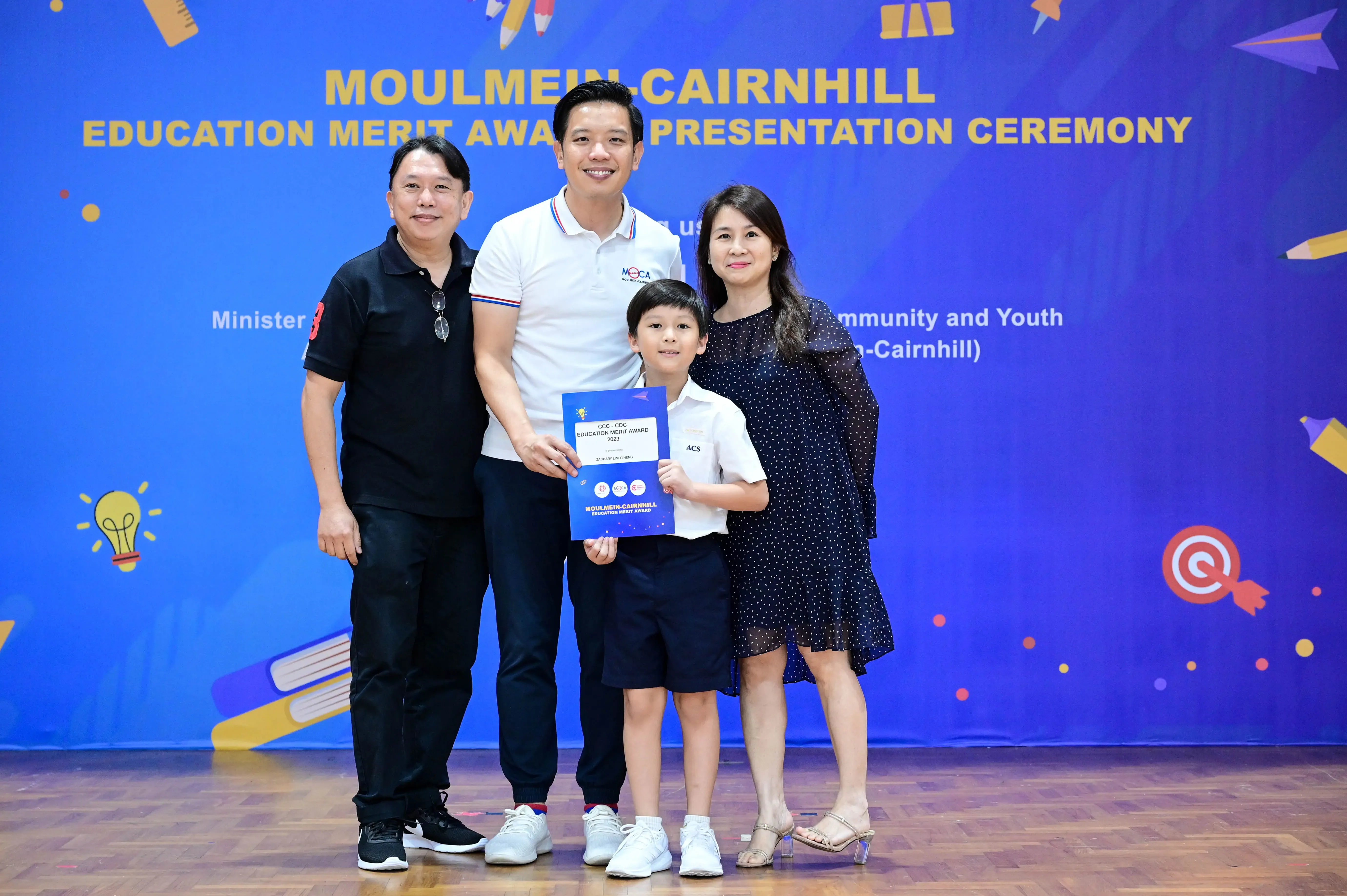 Three adults and a boy holding an award certificate pose at the Moulmein-Cairnhill Education Merit Award Ceremony.