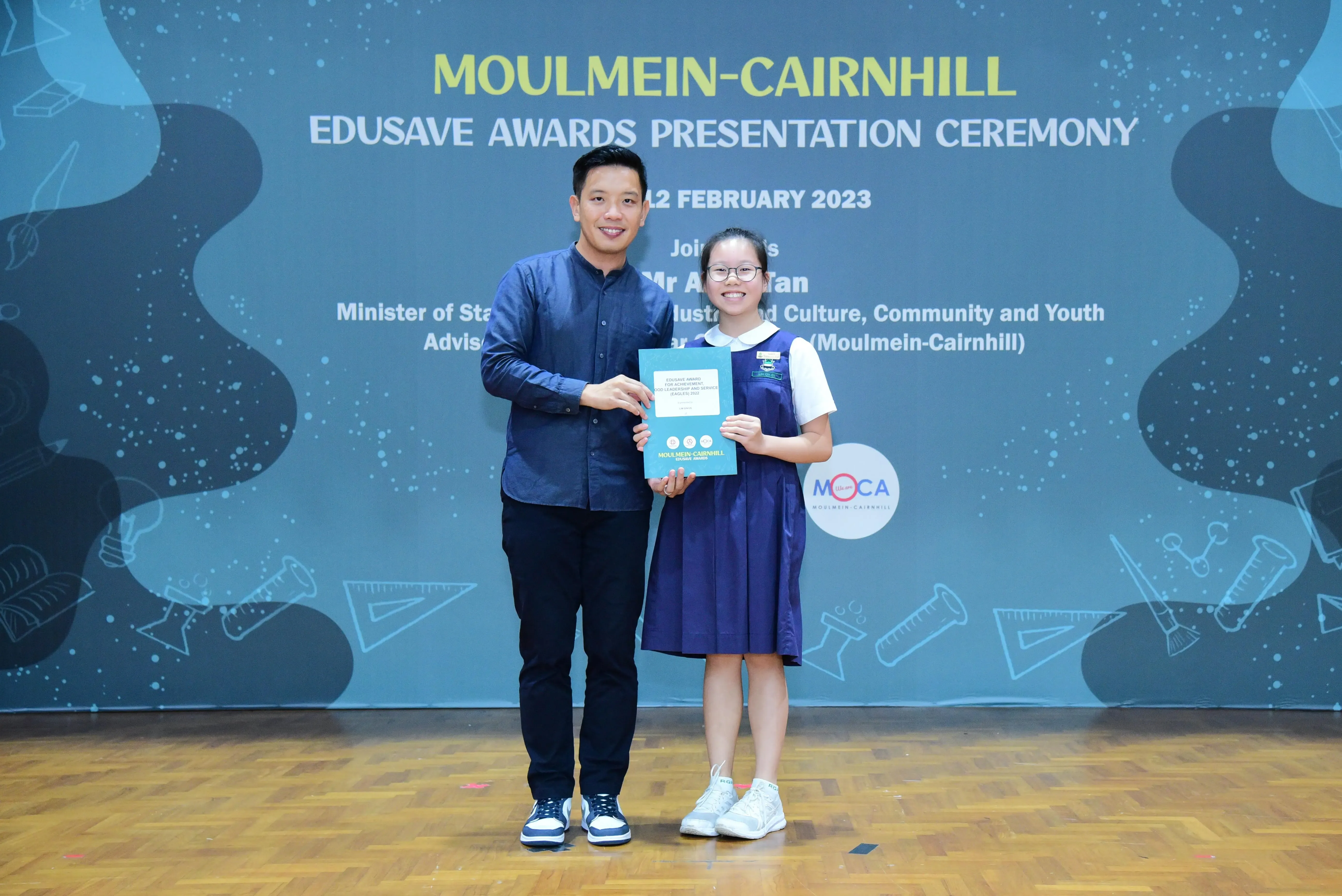 A man and a young girl hold a certificate at the Moulmein-Cairnhill Edusave Awards Presentation Ceremony, February 2023.