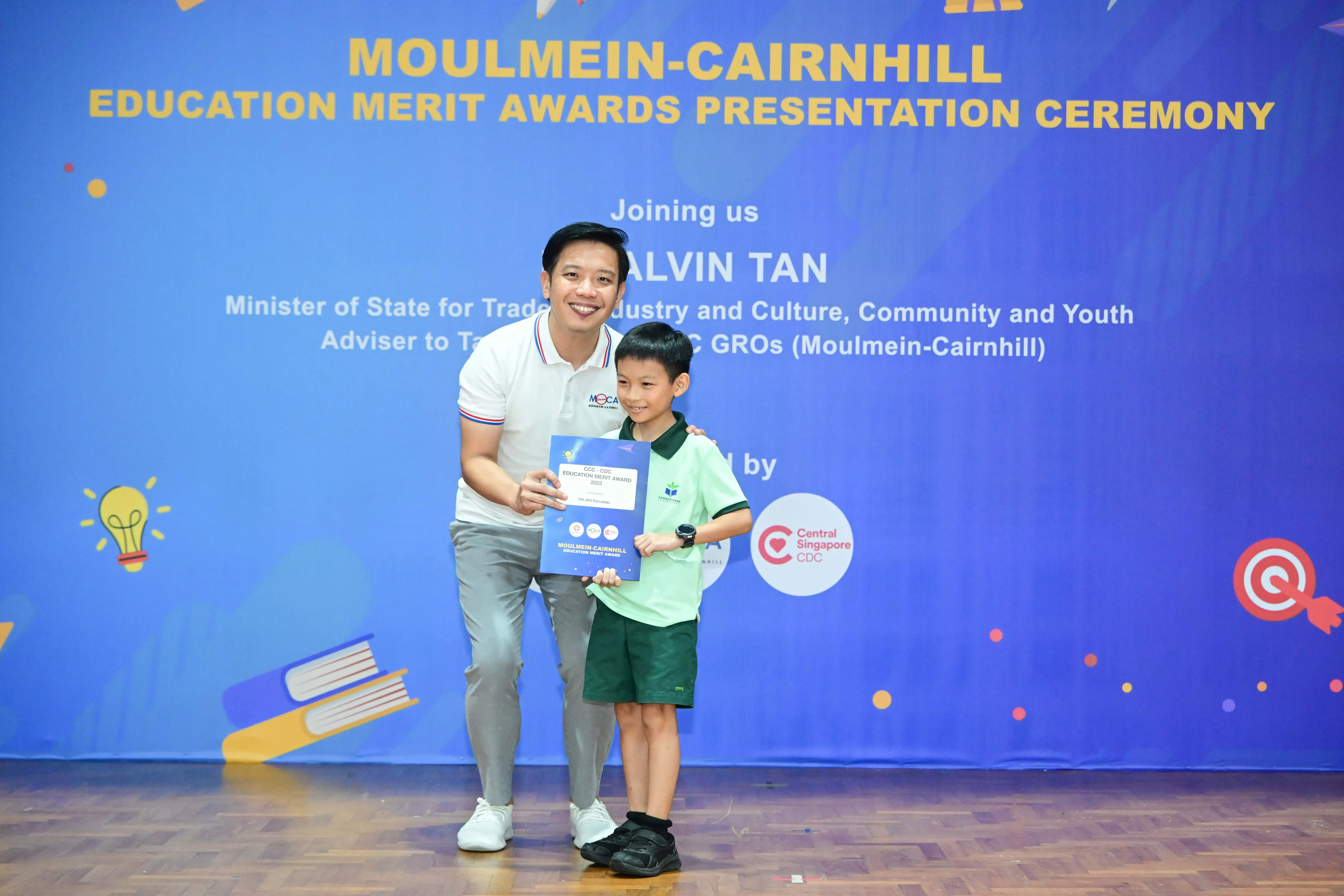 A man and a young boy hold an award certificate at the Moulmein-Cairnhill Education Merit Awards Presentation Ceremony.