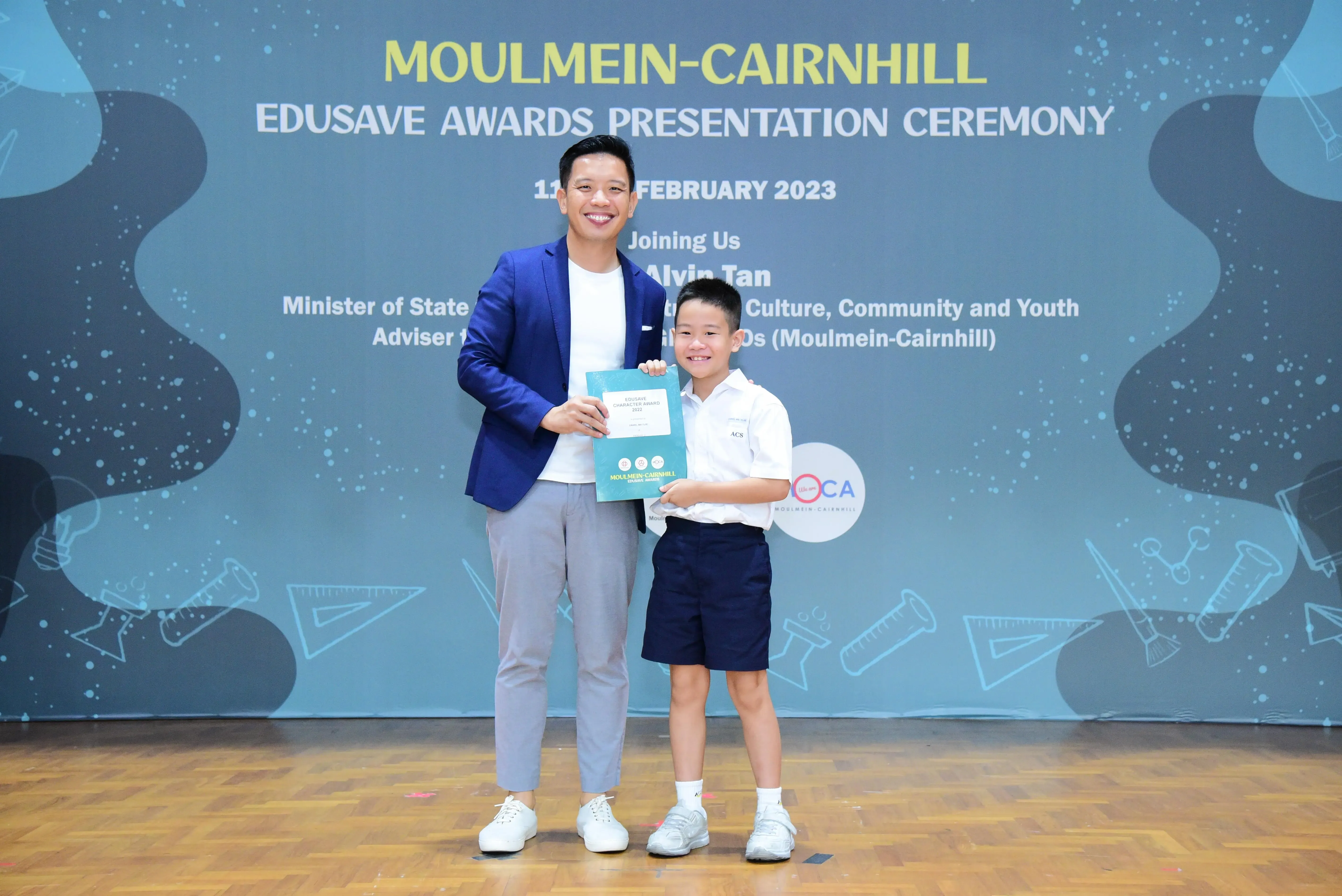 A man in a blue blazer and a young boy in school uniform hold a certificate at the Moulmein-Cairnhill Edusave Awards 2023.