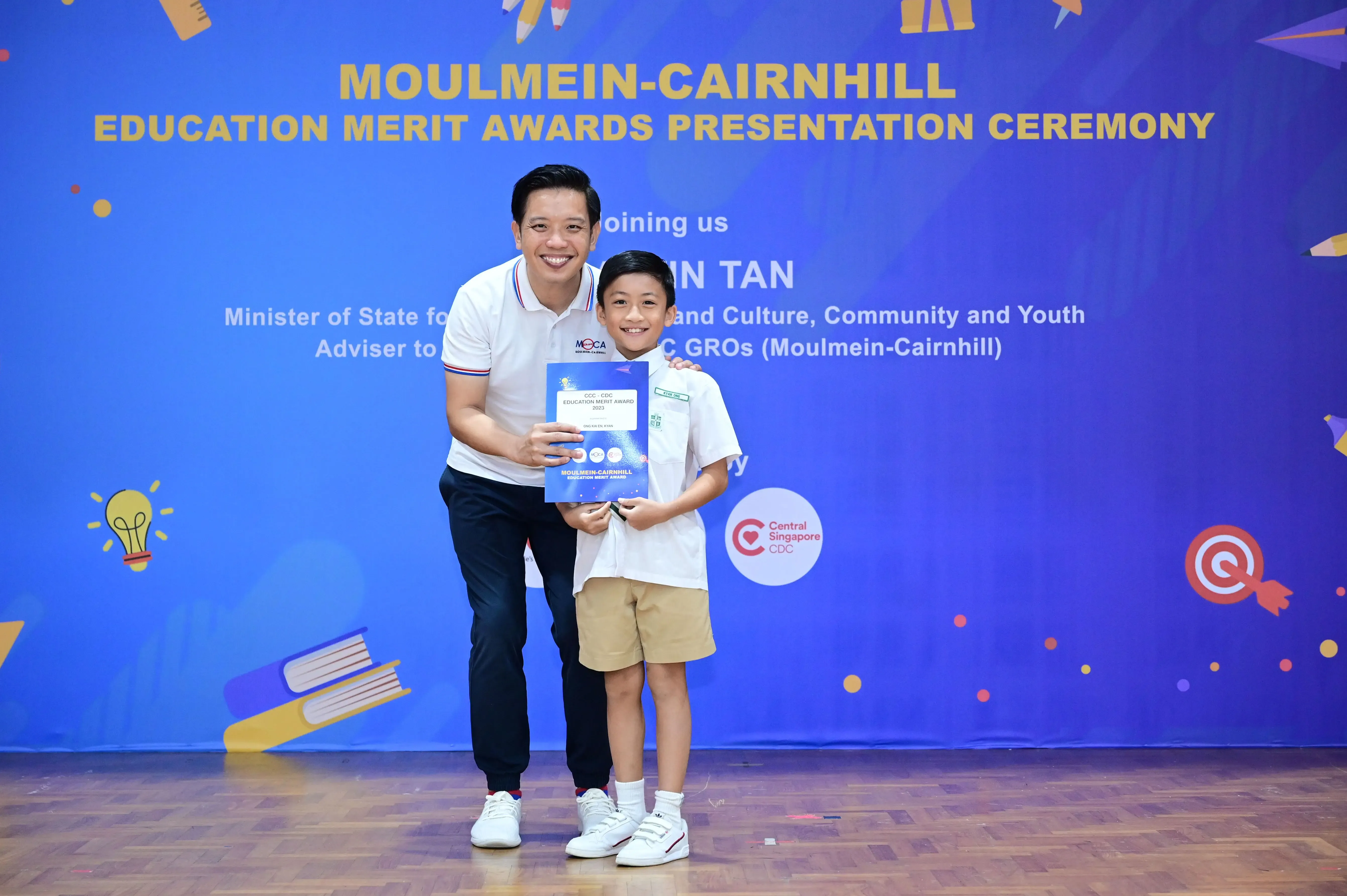 A man and a young boy hold a certificate at the Moulmein-Cairnhill Education Merit Awards Presentation Ceremony.