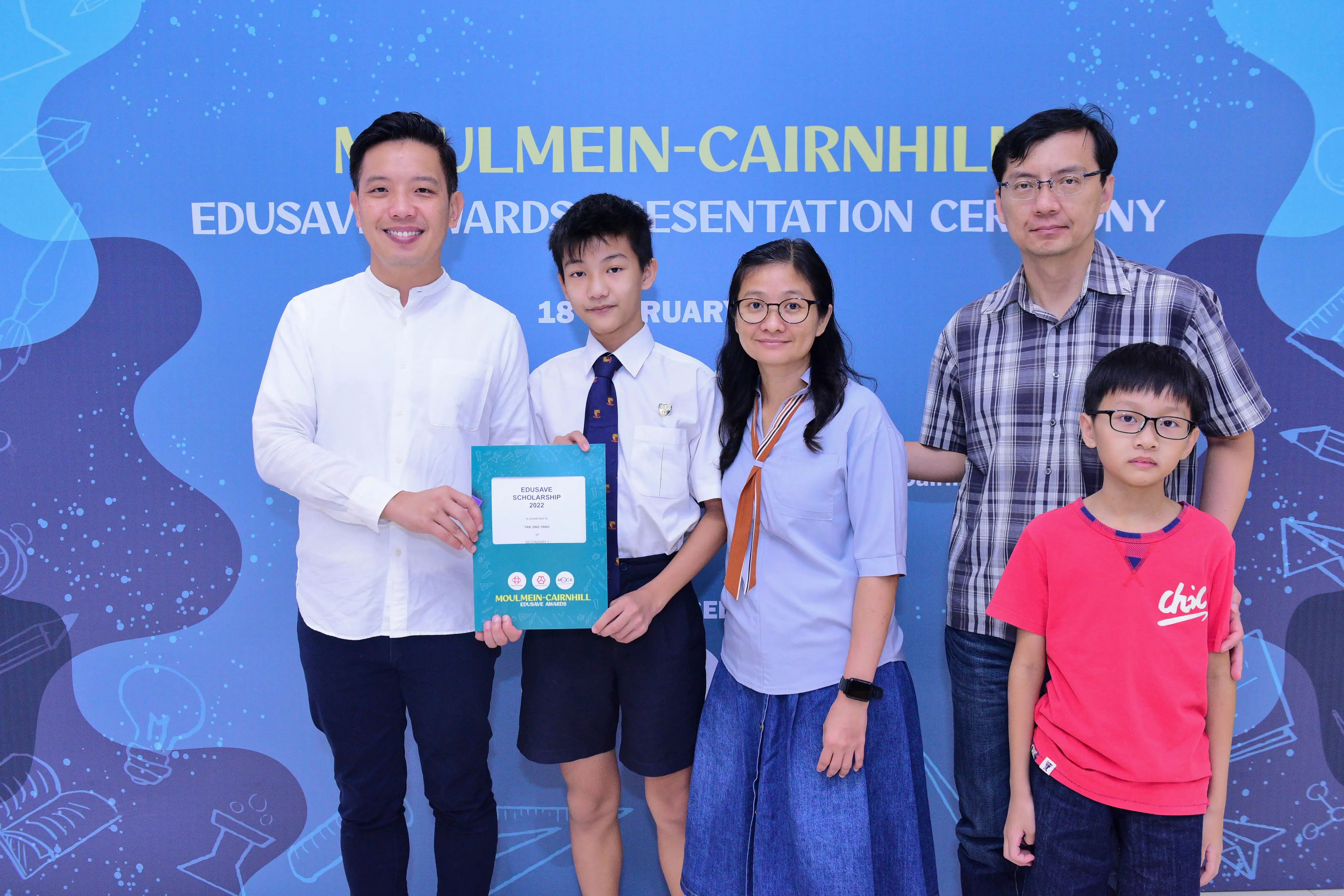 Five people pose at the Moulmein-Cairnhill Edusave Awards Presentation Ceremony, holding a scholarship certificate.