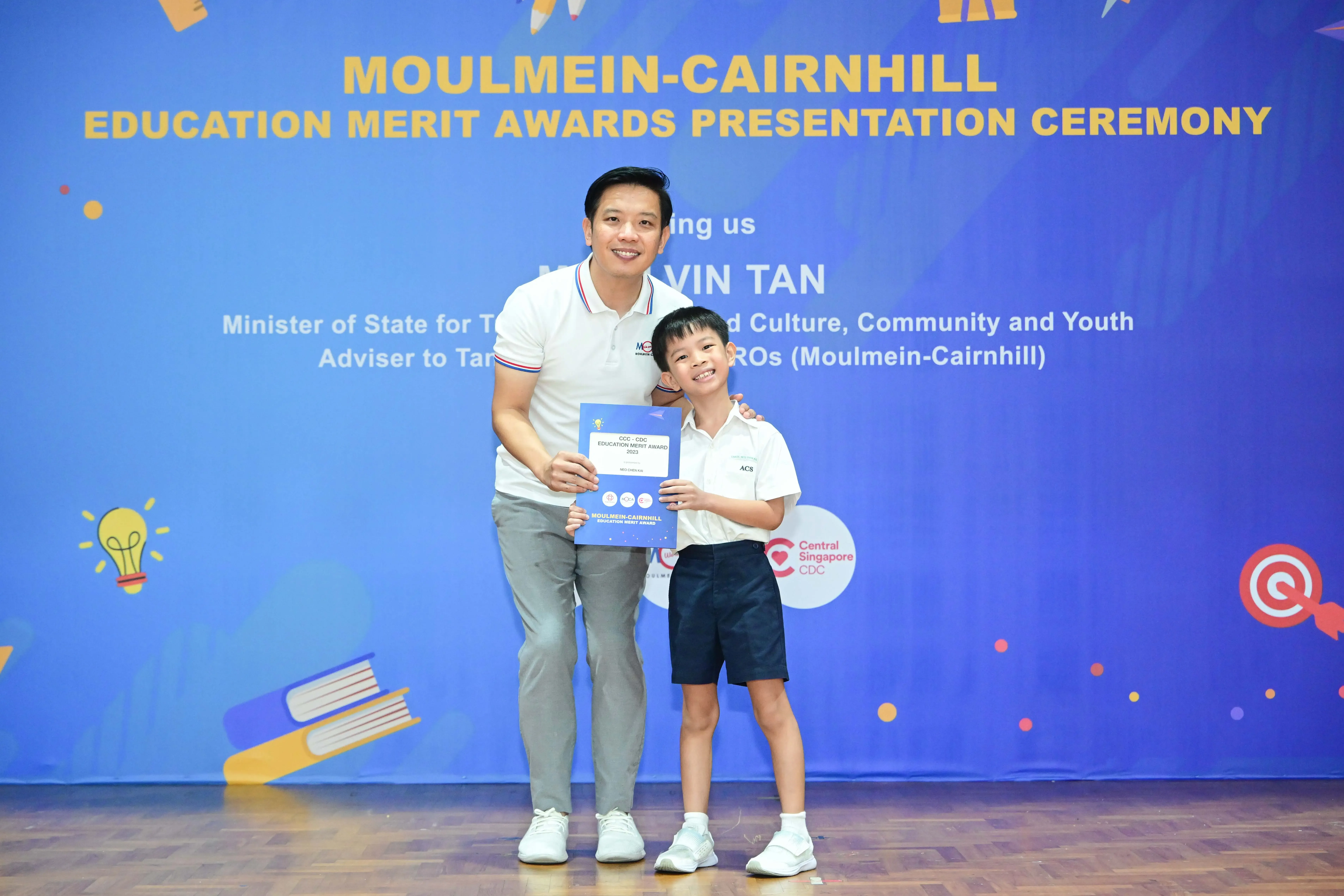 A man and a young boy hold a certificate at the Moulmein-Cairnhill Education Merit Awards Presentation Ceremony.