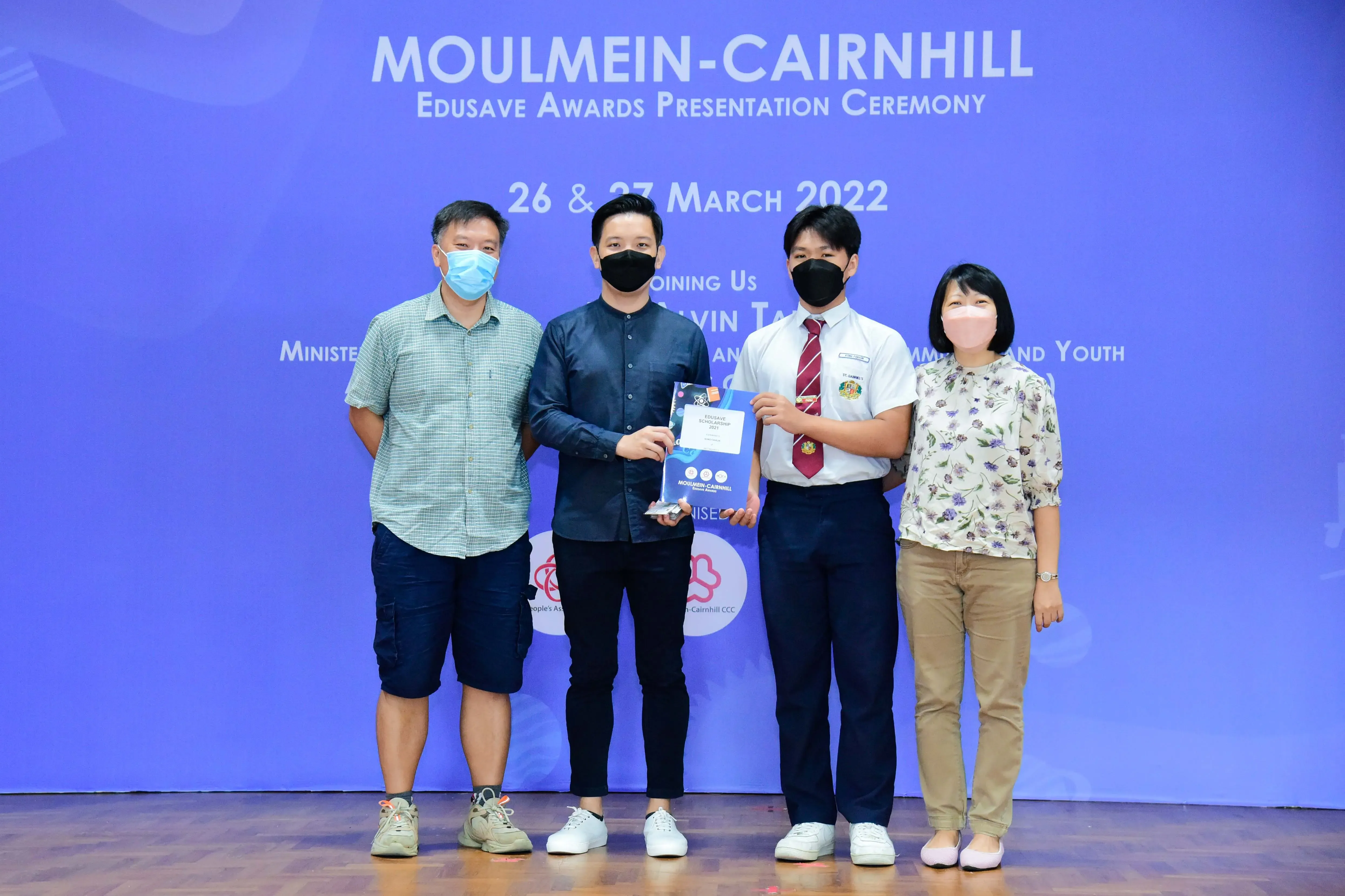 Four masked people stand on a stage at the Moulmein-Cairnhill Edusave Awards Presentation Ceremony, March 2022.