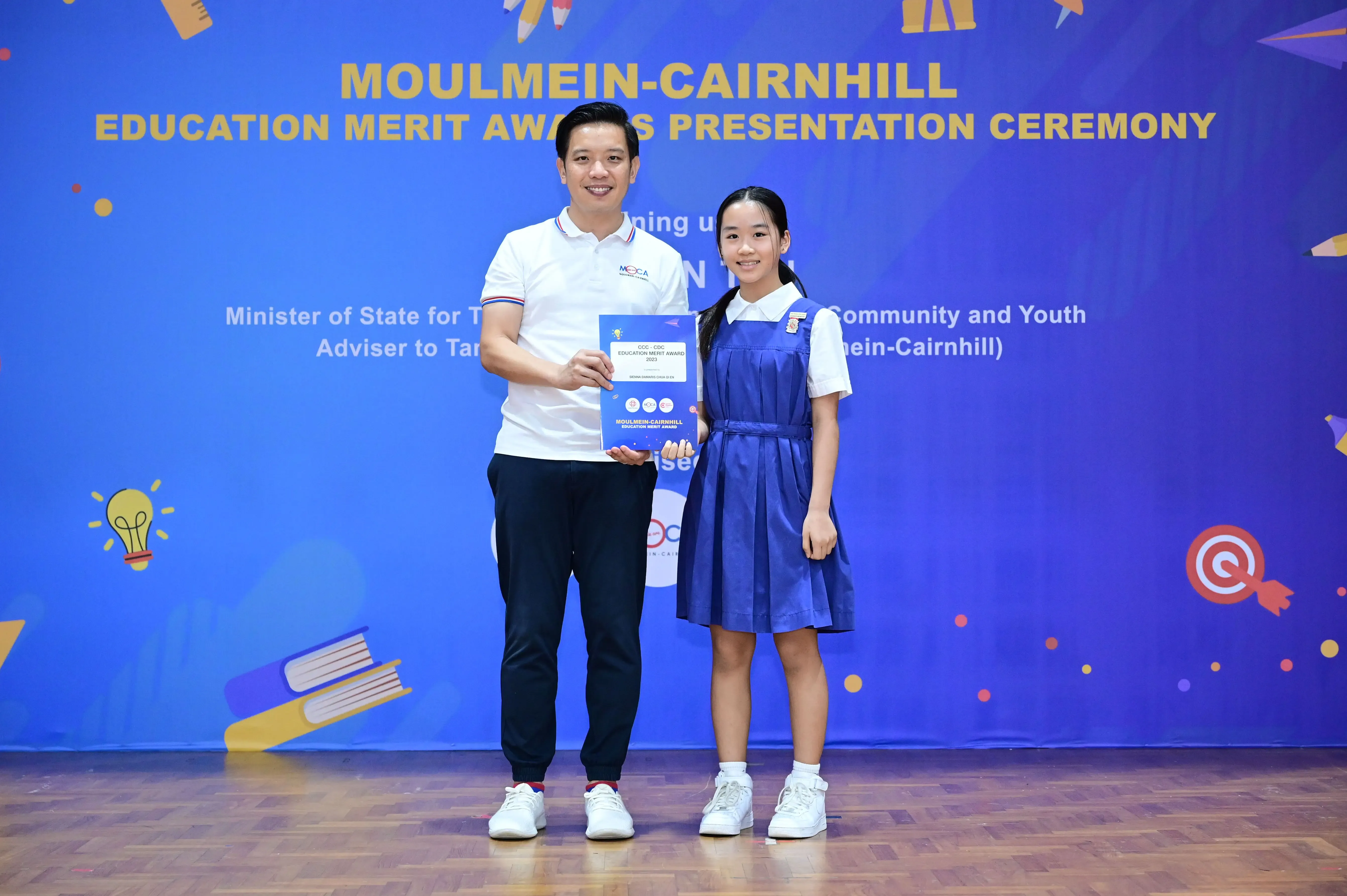 A man and a girl in school uniform hold an award certificate at the Moulmein-Cairnhill Education Merit Awards ceremony.