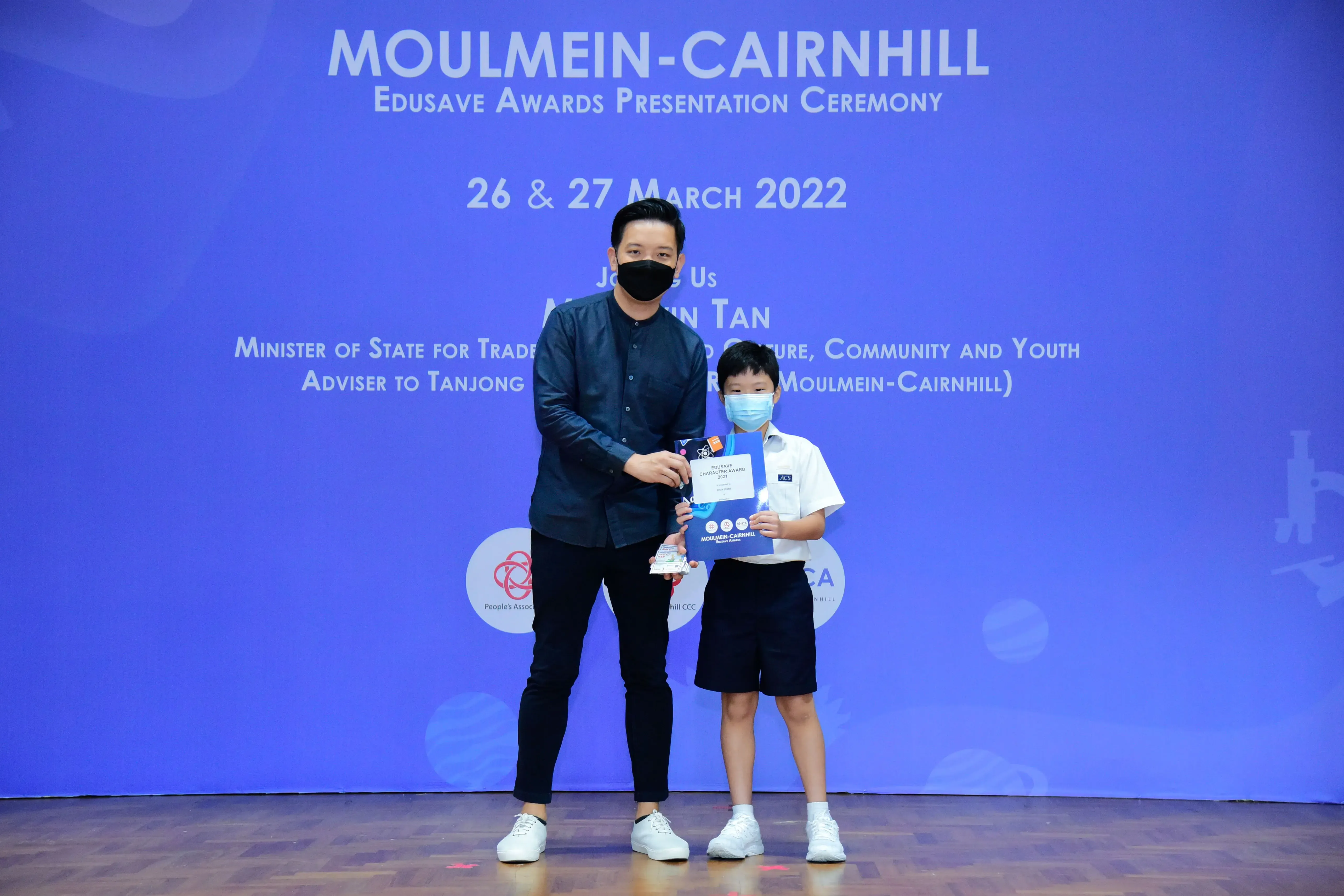An adult and a young boy in masks hold an award at the Moulmein-Cairnhill Edusave Awards Ceremony, March 2022.
