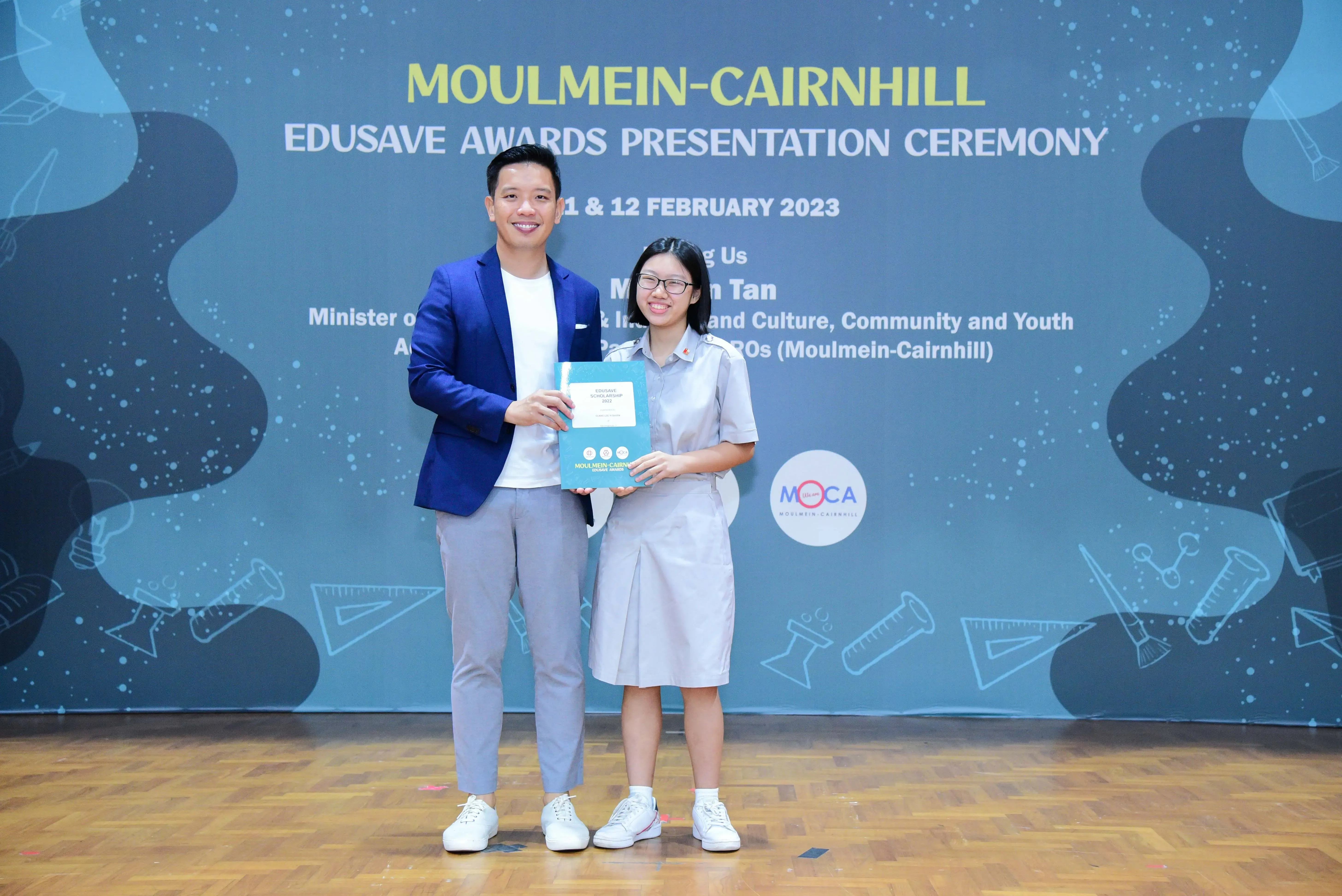 A man in a blue blazer and a girl in school uniform hold an award at the Moulmein-Cairnhill Edusave ceremony.