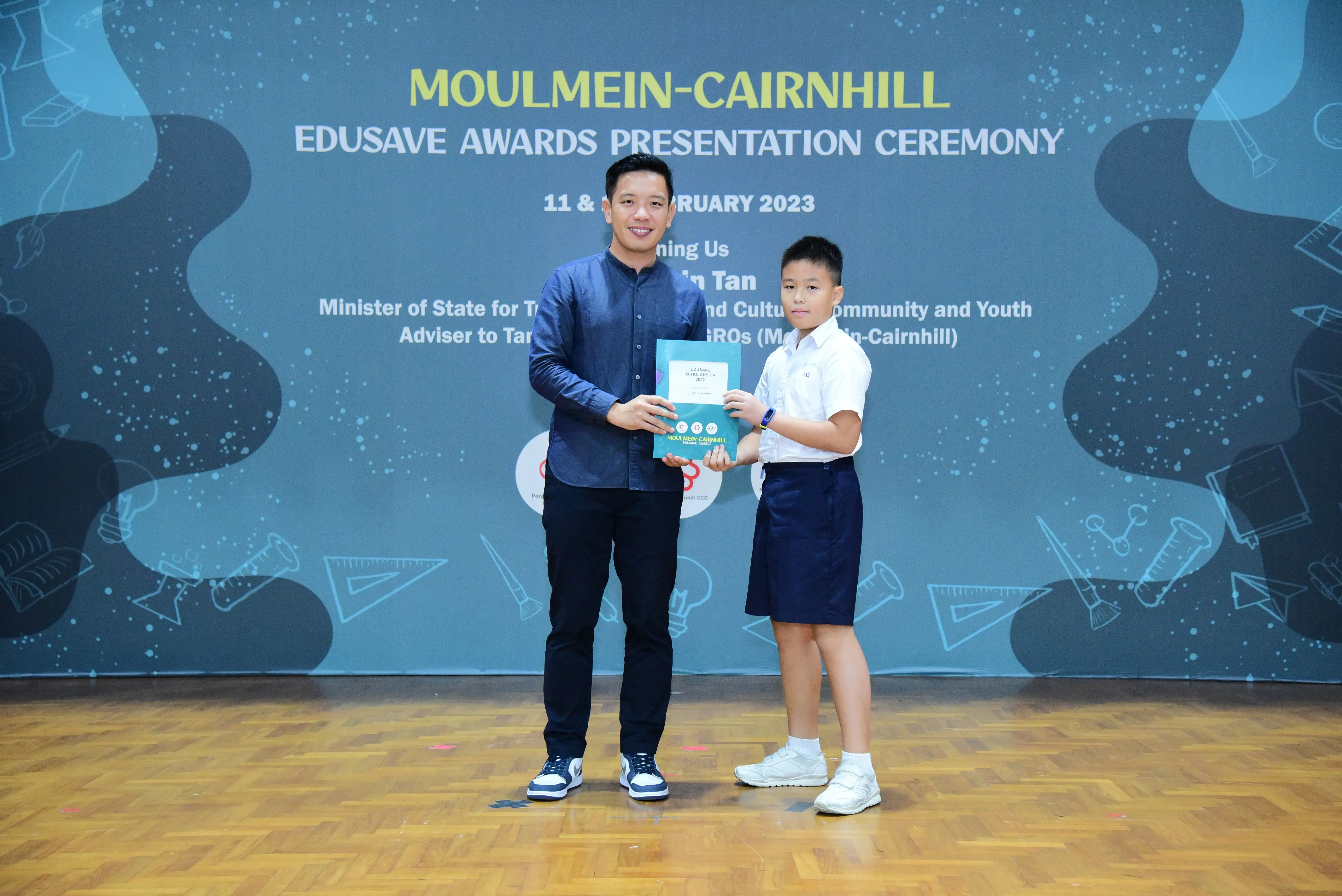 An adult and a young student hold an award together at the Moulmein-Cairnhill Edusave Awards Ceremony 2023.