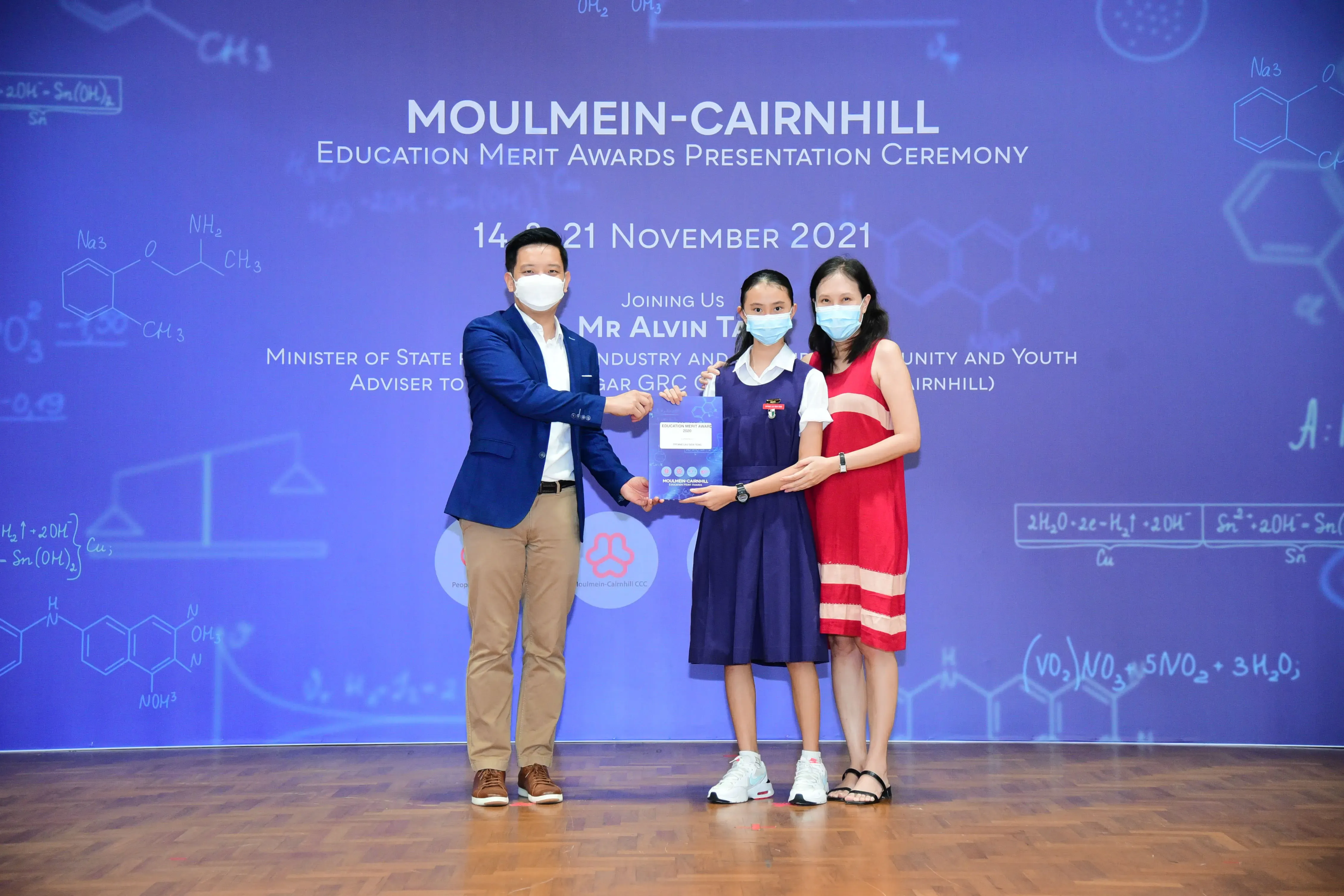 Three masked people pose on stage at the Moulmein-Cairnhill Education Merit Awards Ceremony, November 2021.