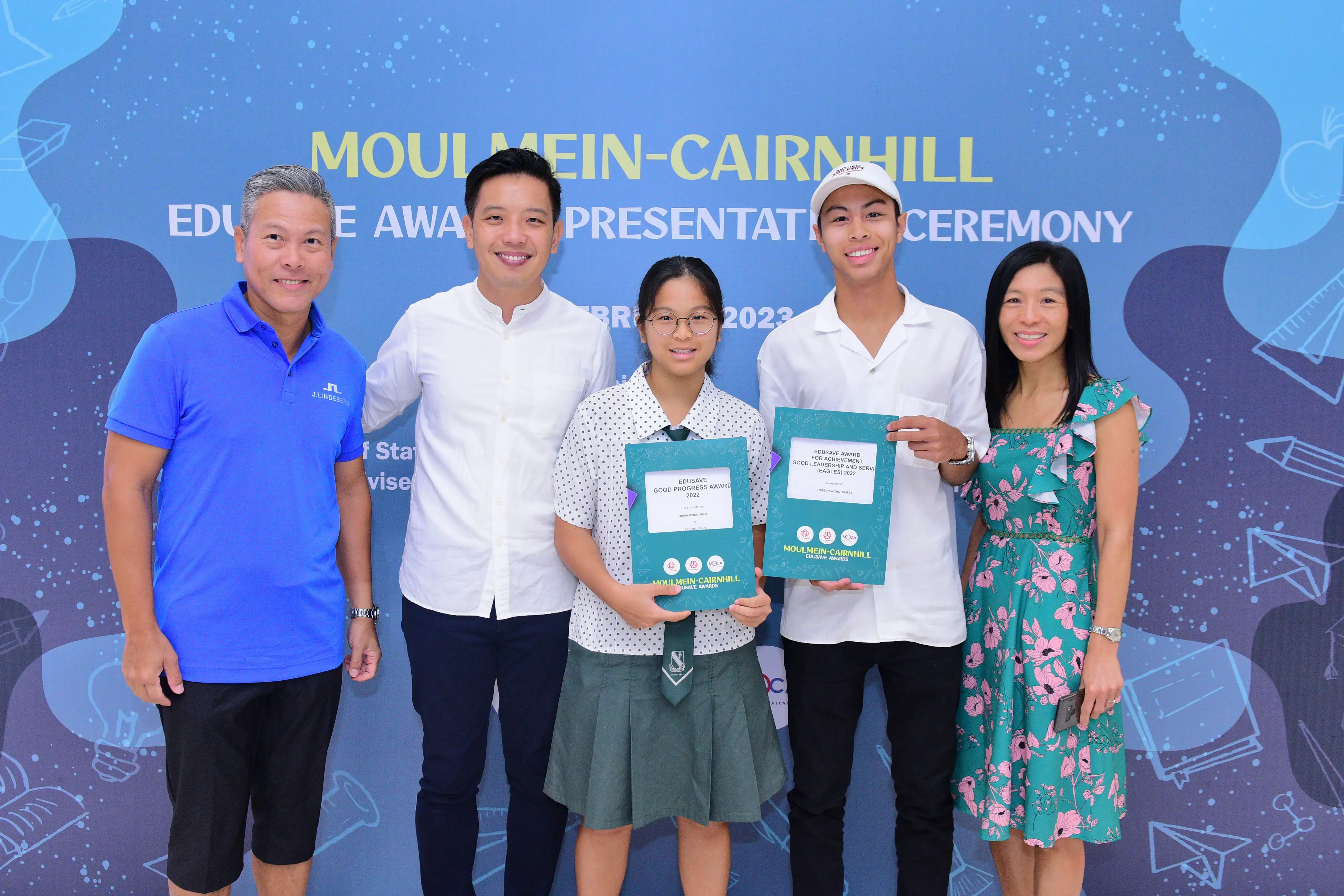 Five people smile at the Moulmein-Cairnhill Edusave Award Presentation Ceremony 2023, two students holding award certificates.