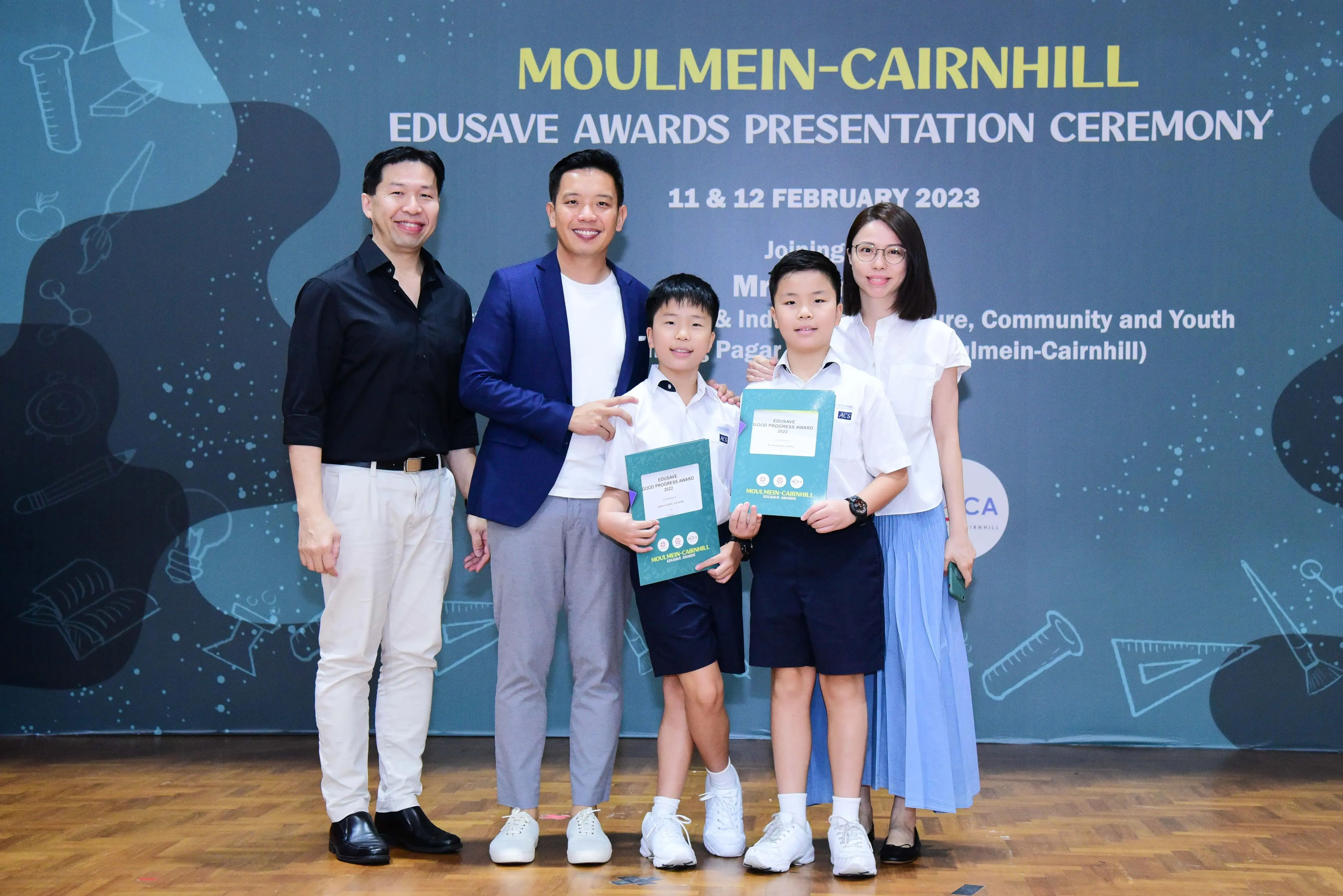 Two adults and two boys holding award folders pose at the Moulmein-Cairnhill Edusave Awards Ceremony, February 2023.