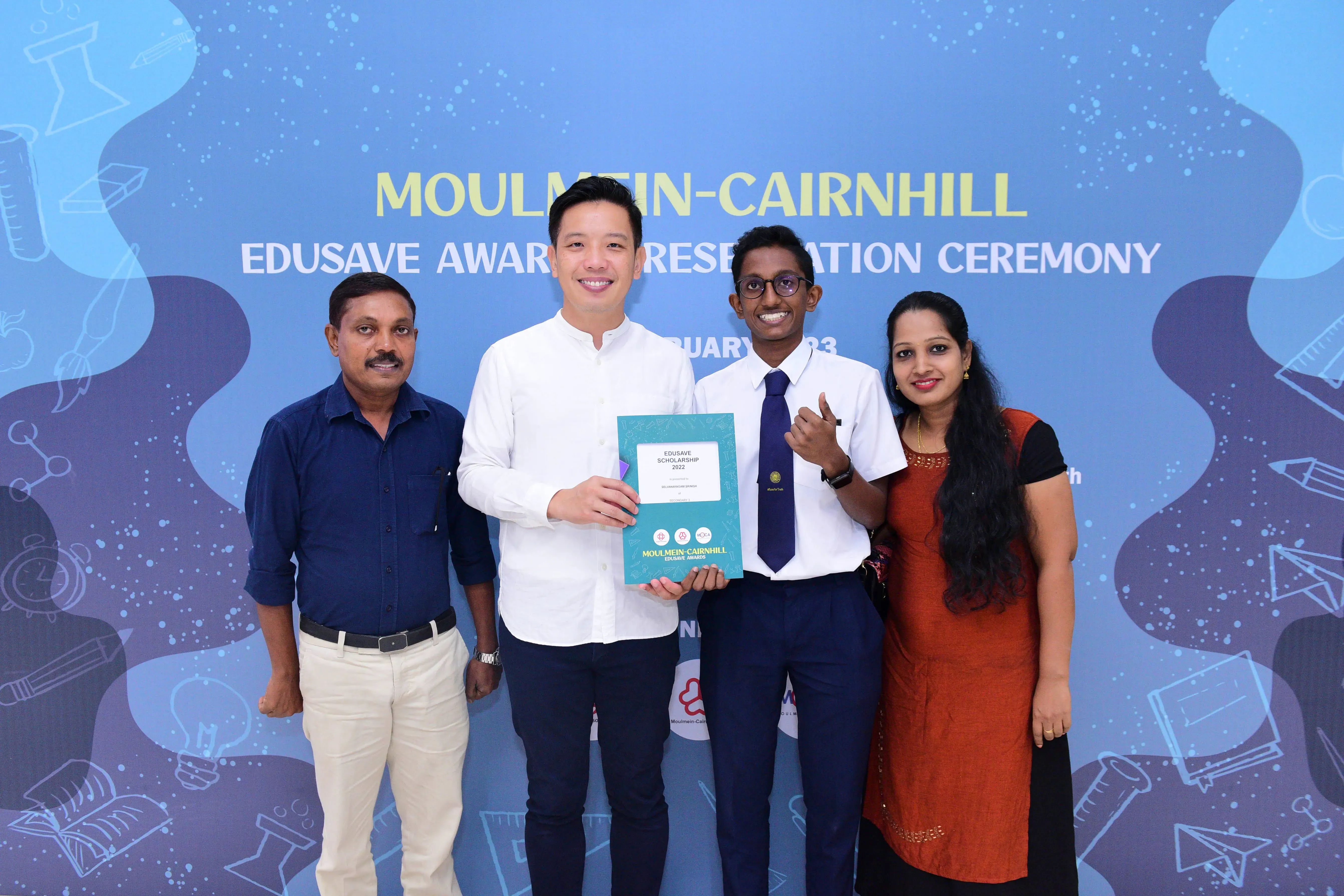 Four people smile at the Moulmein-Cairnhill Edusave Awards Presentation Ceremony, holding a scholarship certificate.