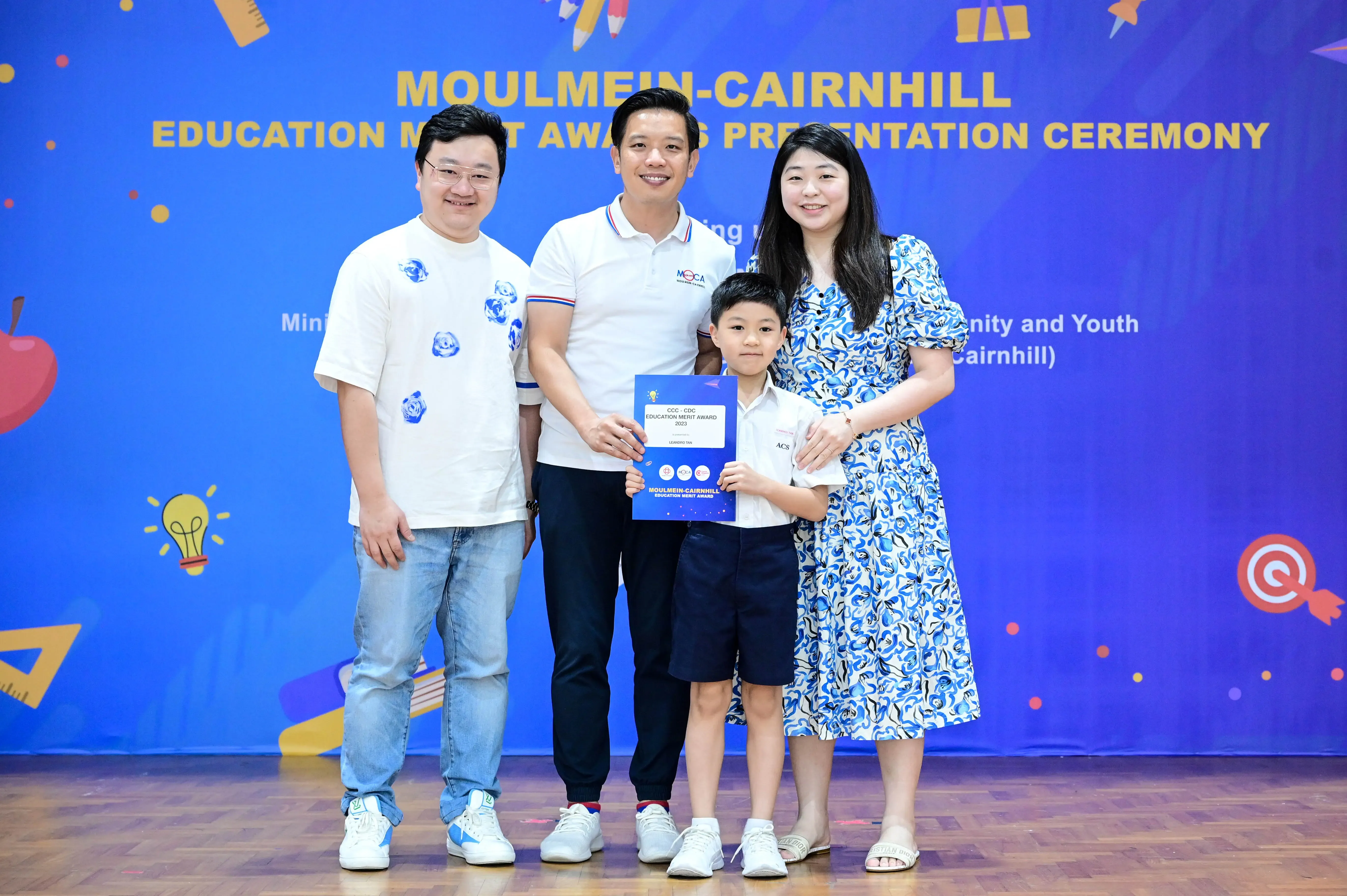 Three adults and a young boy pose with an award certificate at the Moulmein-Cairnhill Education Merit Awards Ceremony.