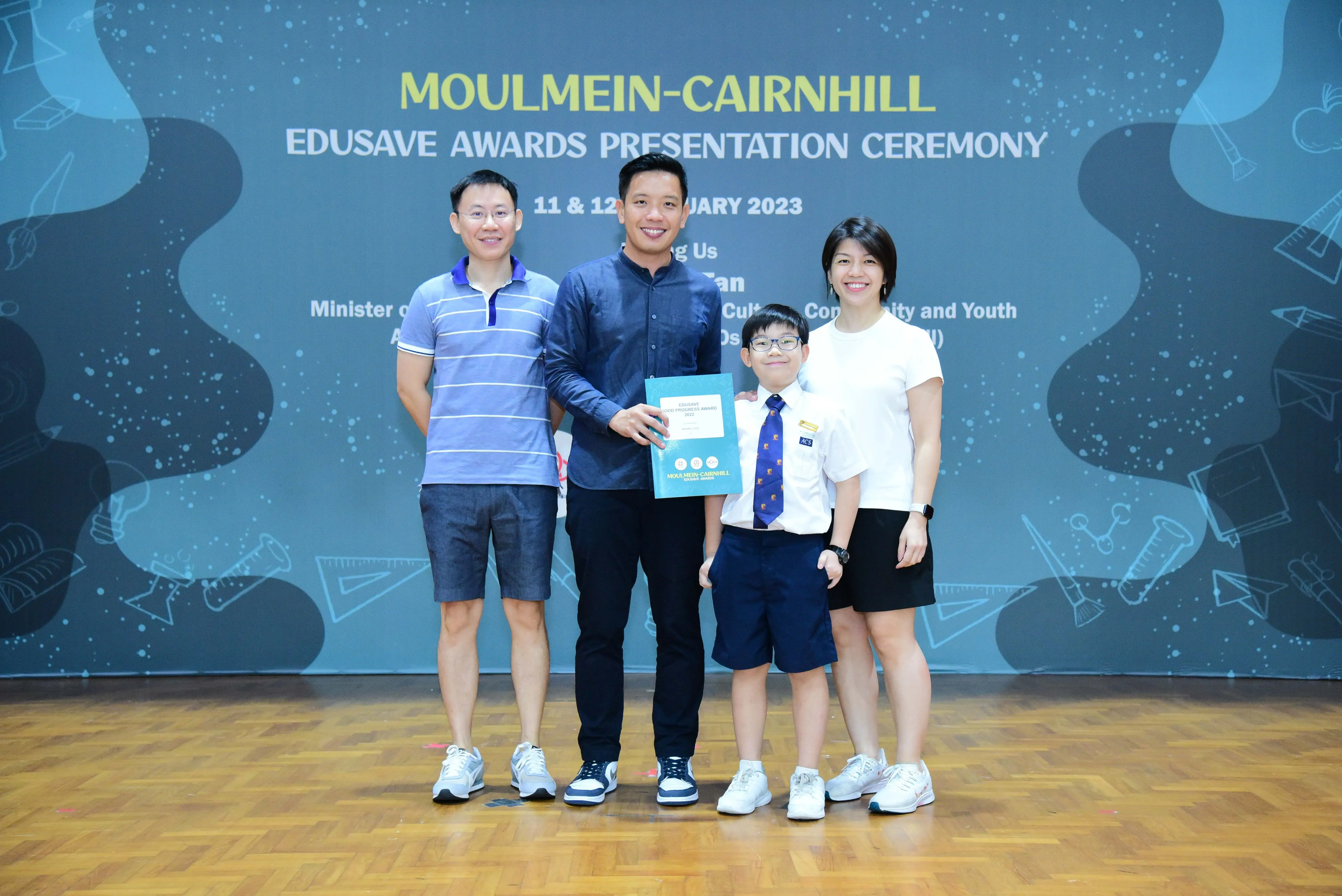 Four people pose at the Moulmein-Cairnhill Edusave Awards Presentation Ceremony 2023, including a young boy in uniform.