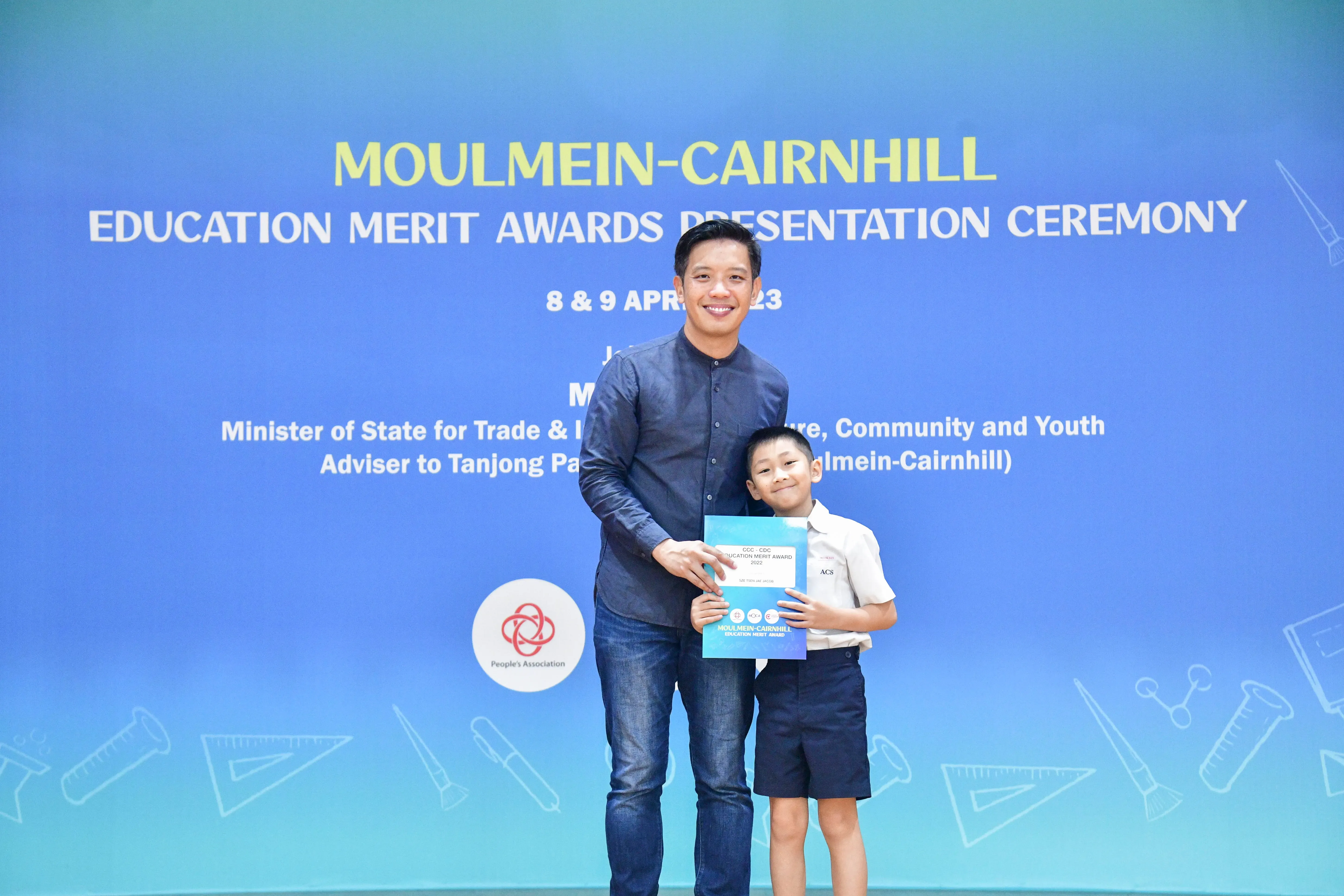 A man and a young boy hold a certificate together at the Moulmein-Cairnhill Education Merit Awards ceremony.