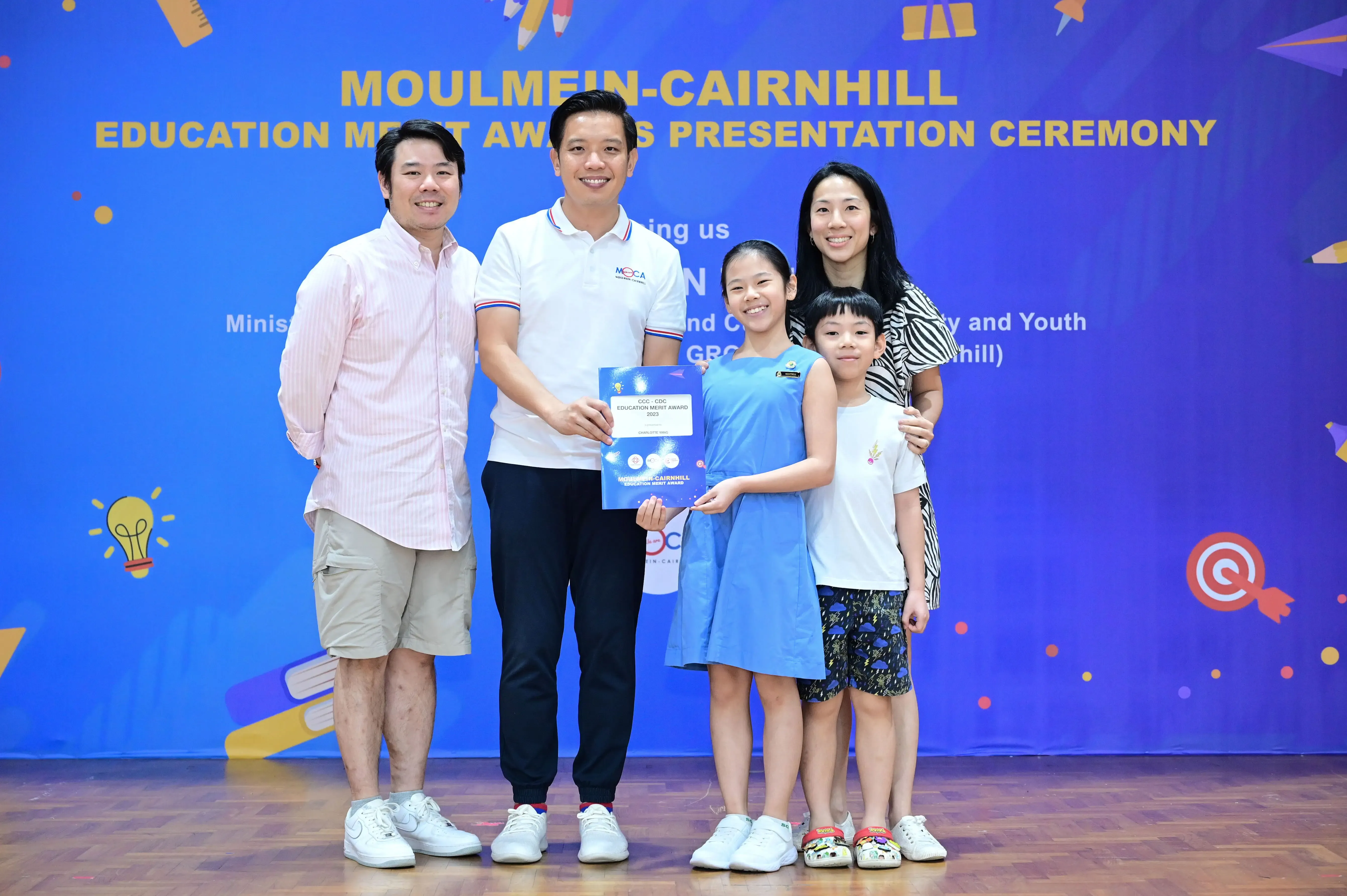 Two adults and two children pose with an award certificate at the Moulmein-Cairnhill Education Merit Awards Presentation Ceremony.