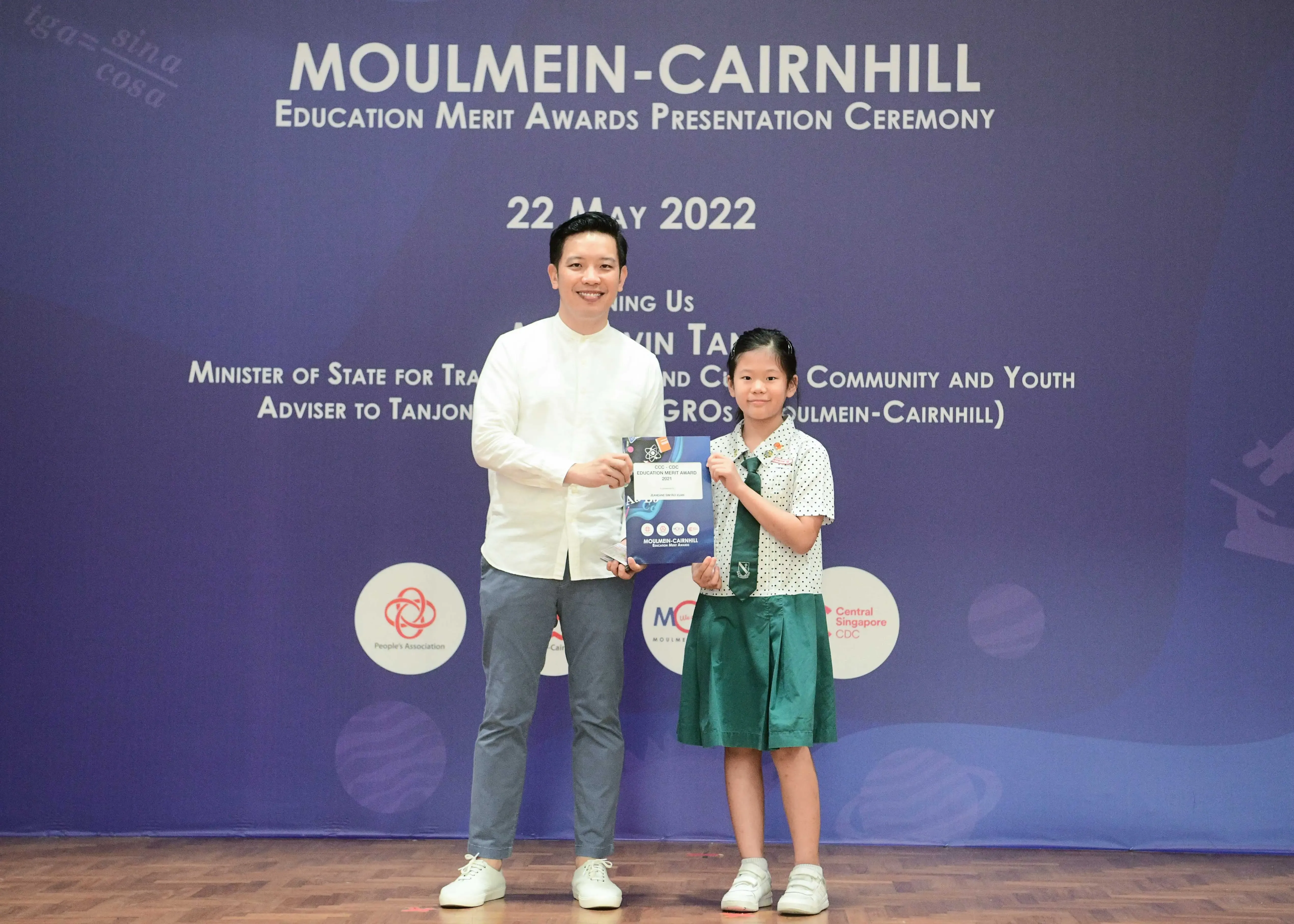 A man and a young girl in school uniform hold an award at the Moulmein-Cairnhill Education Merit Awards ceremony on 22 May 2022.