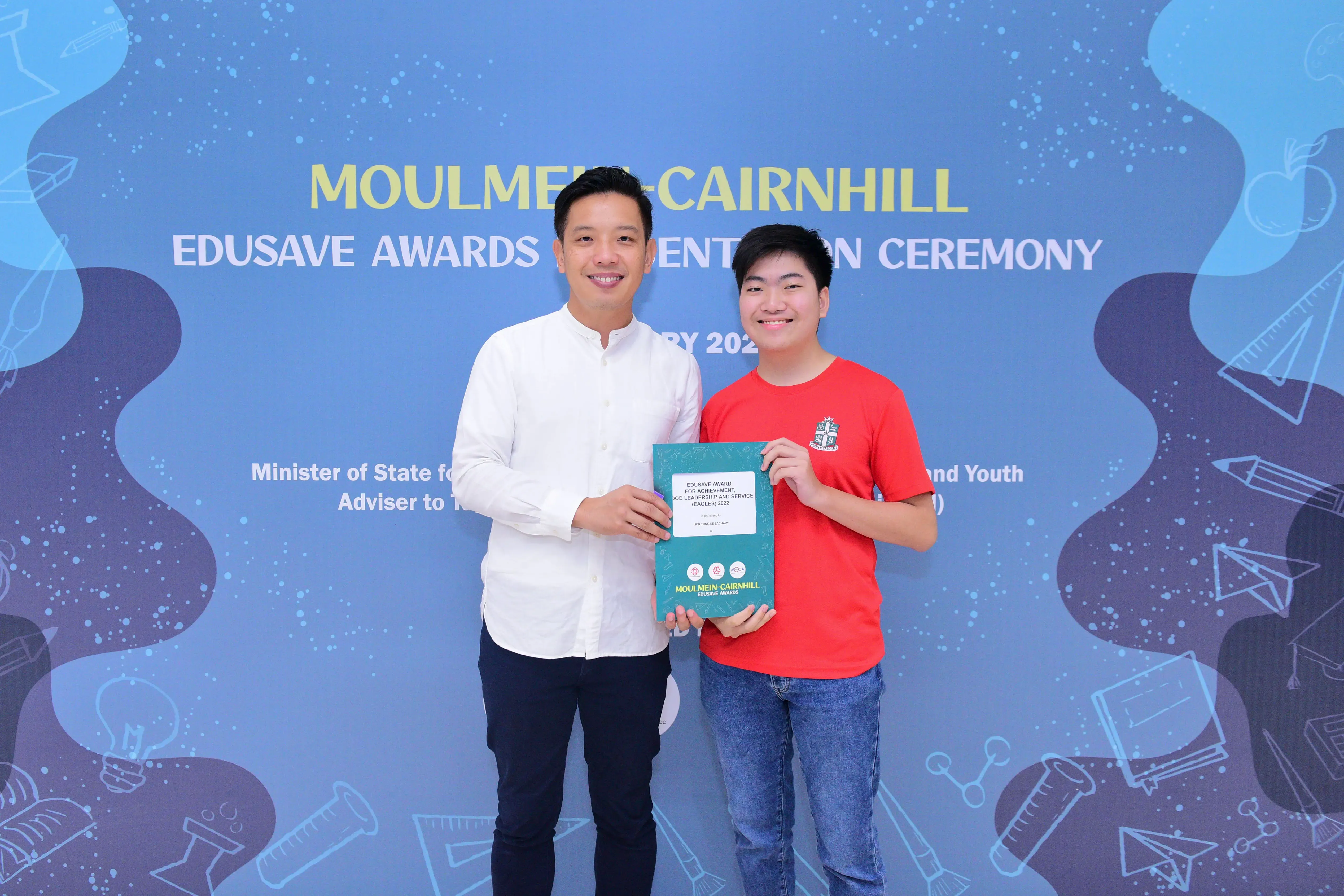 Two smiling people hold a certificate together at the Moulmein-Cairnhill Edusave Awards Presentation Ceremony.
