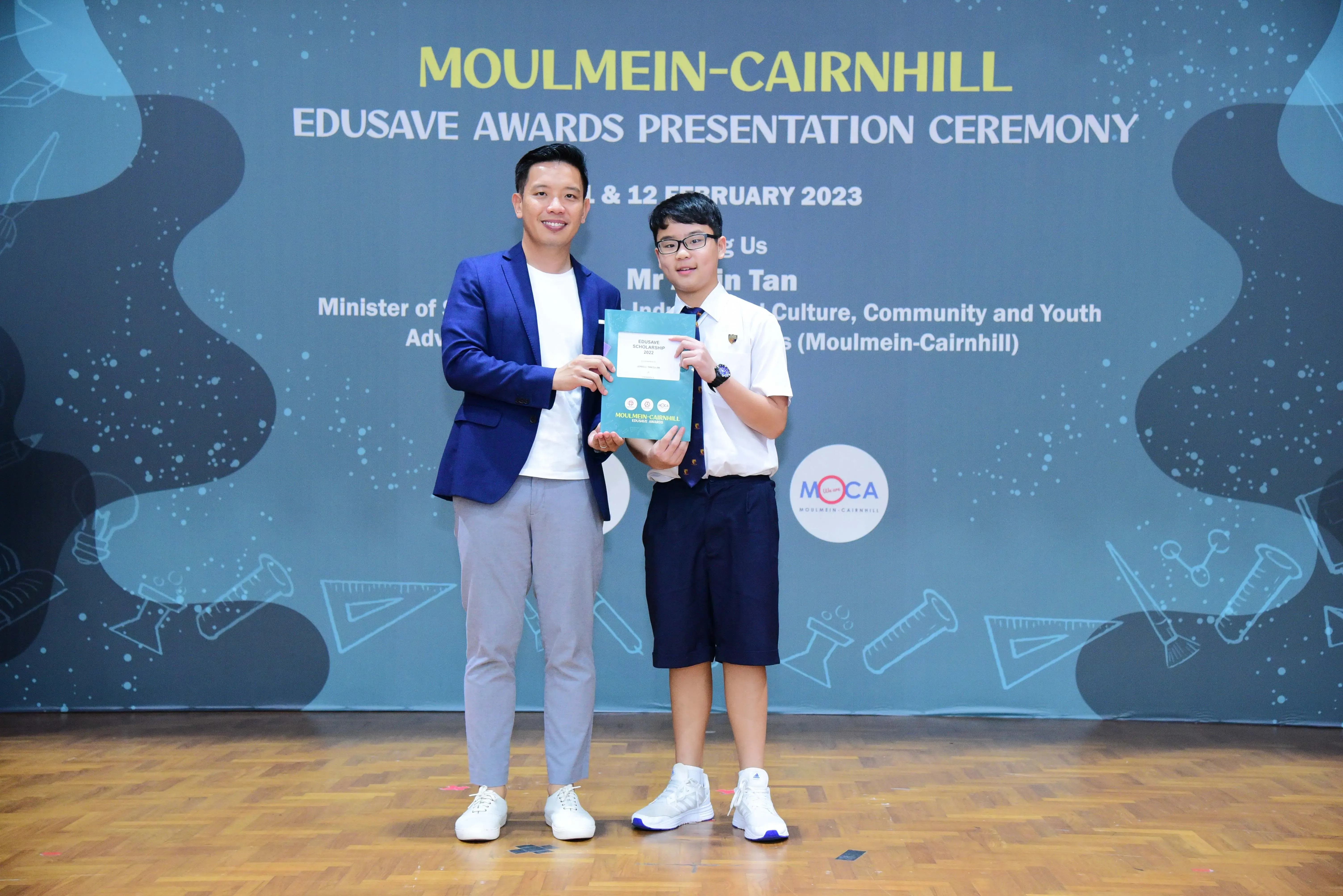 Two people hold an award booklet at the Moulmein-Cairnhill Edusave Awards Presentation Ceremony, February 2023.