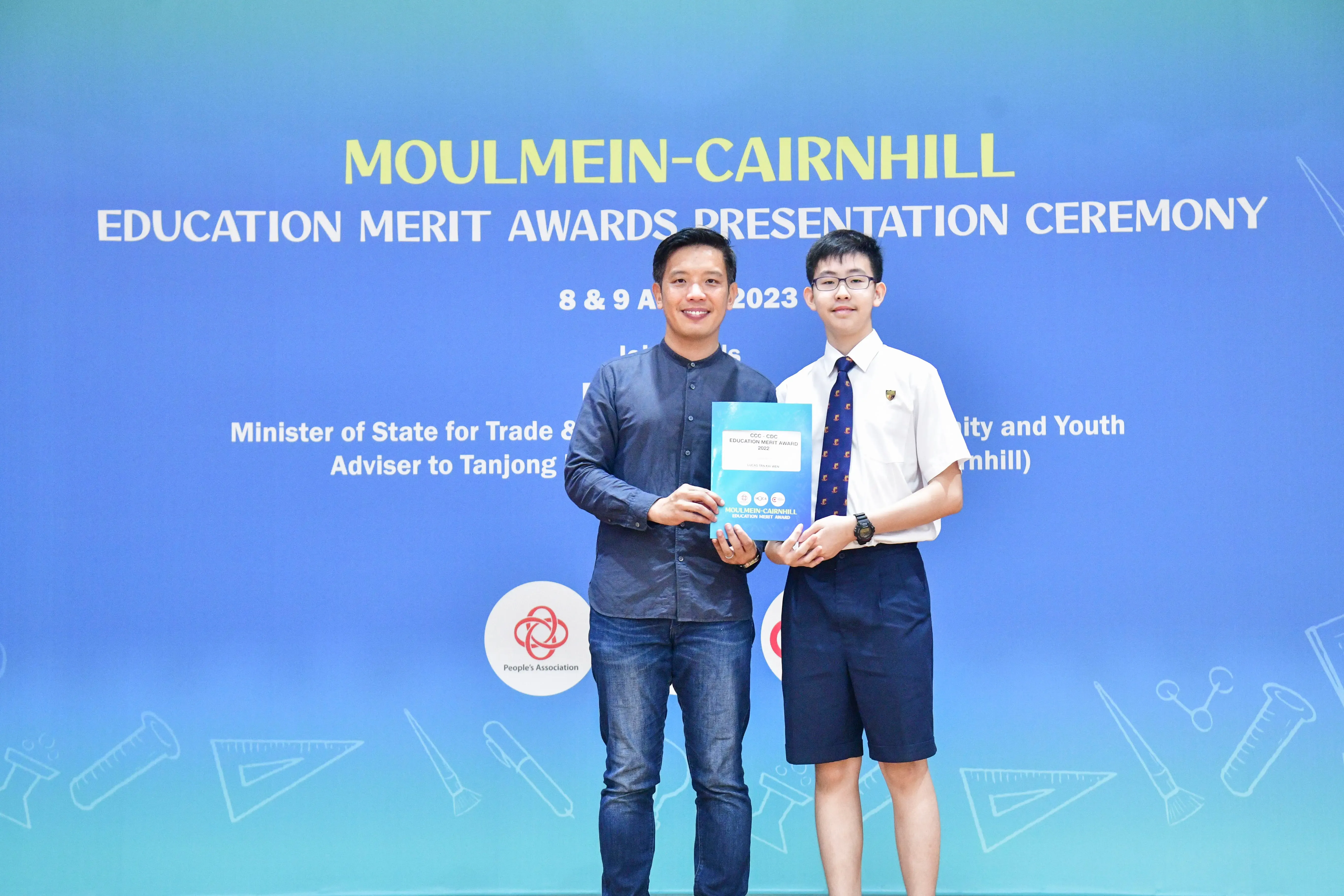 Two people hold an award booklet at the Moulmein-Cairnhill Education Merit Awards Presentation Ceremony 2023.