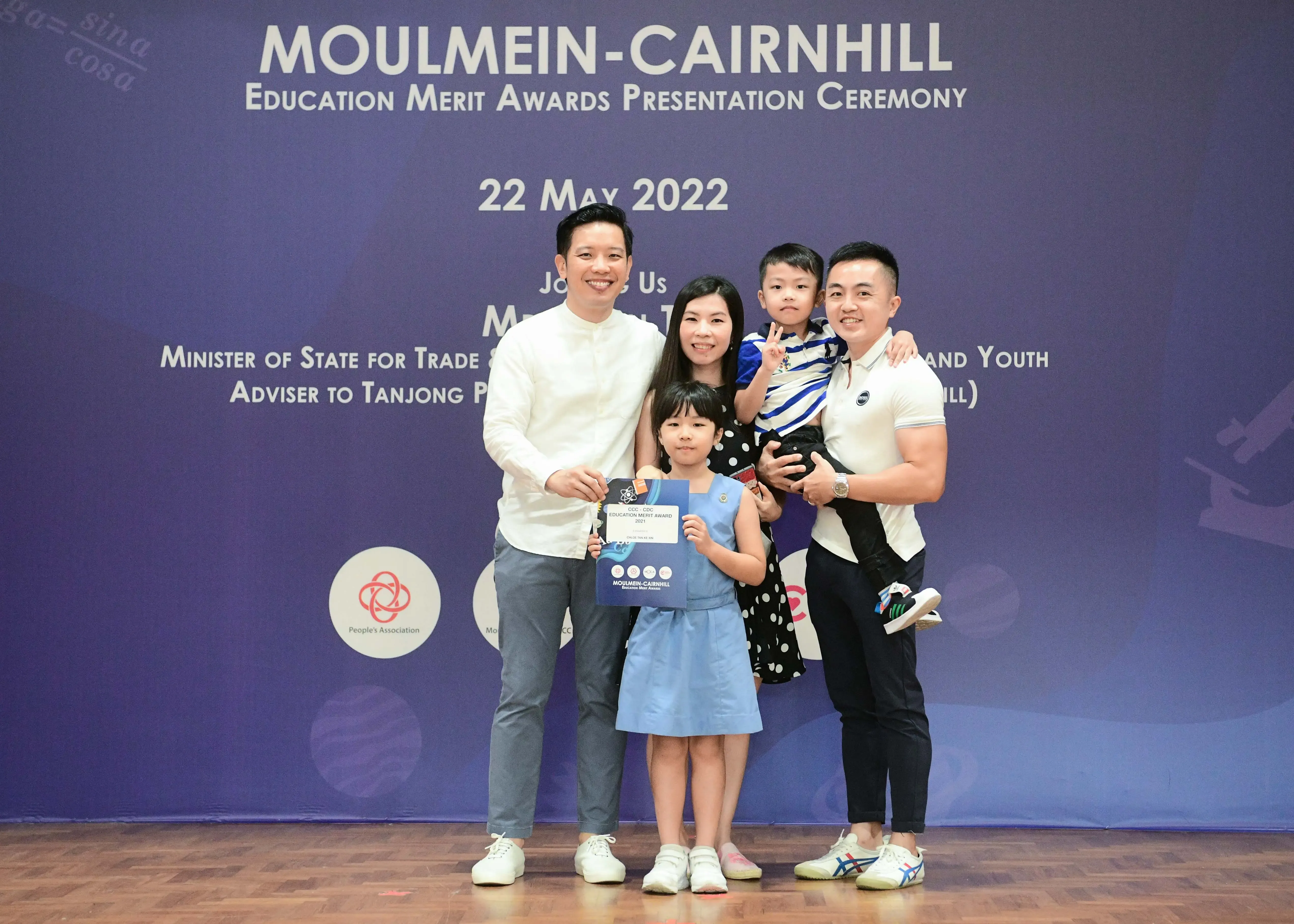 Family of four poses at Moulmein-Cairnhill Education Merit Awards Ceremony on 22 May 2022, girl holds certificate.