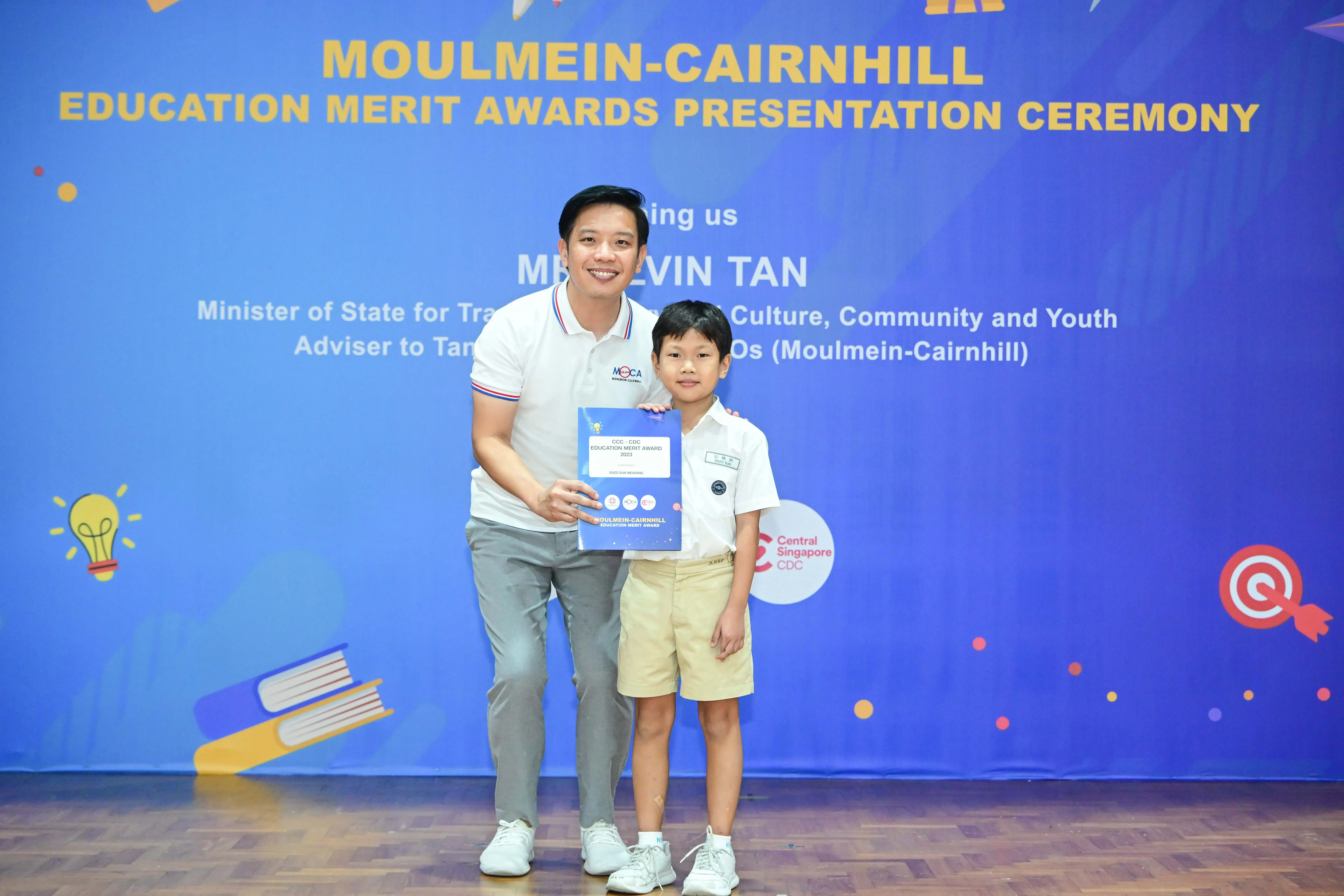 A man and a young boy hold an award certificate at the Moulmein-Cairnhill Education Merit Awards Presentation Ceremony.
