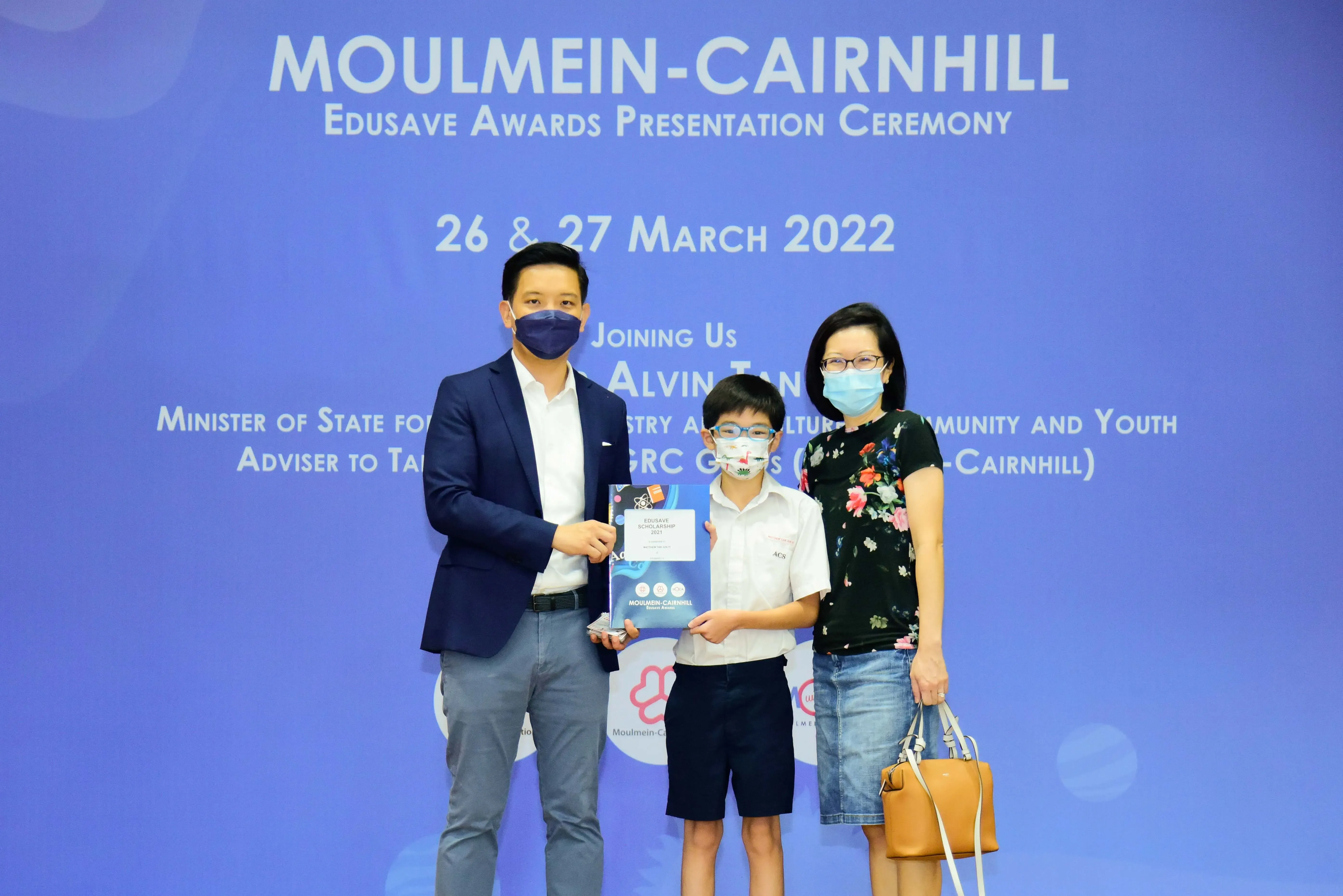 A man, a young boy holding an award certificate, and a woman pose at the Moulmein-Cairnhill Edusave Awards Ceremony.