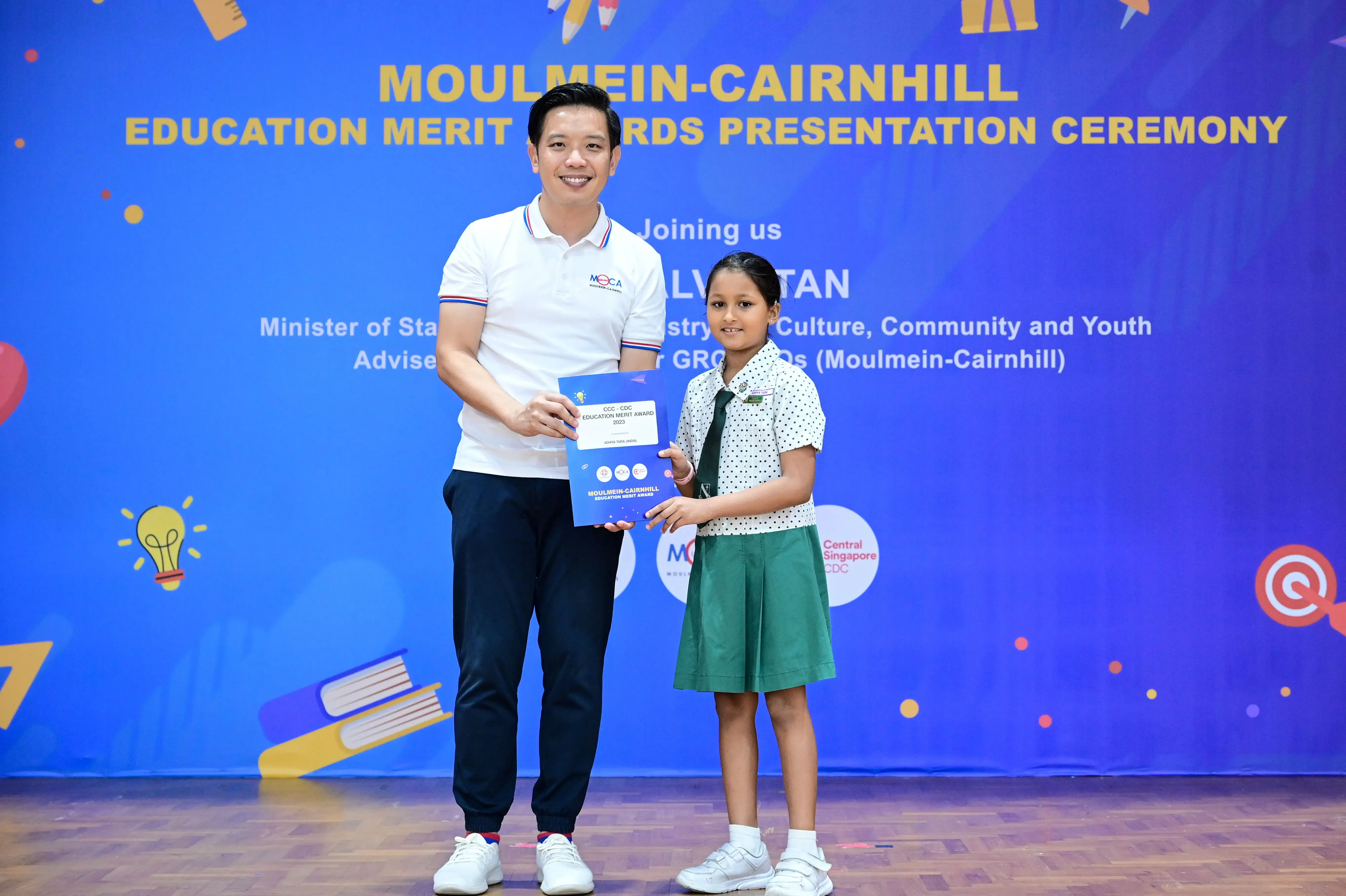 A man and a young girl hold a certificate together at the Moulmein-Cairnhill Education Merit Awards Presentation Ceremony.