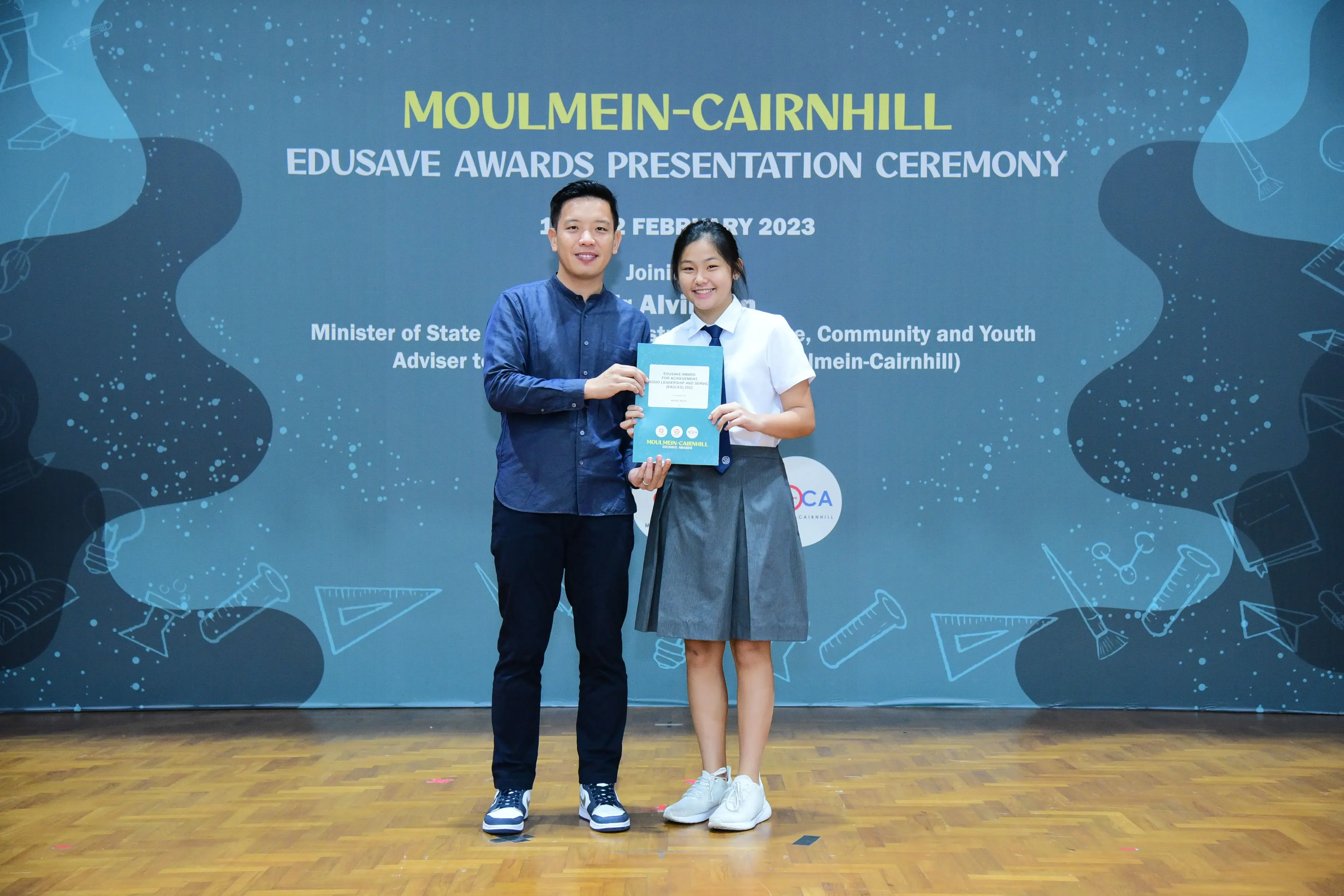 A man and a female student hold an award booklet at the Moulmein-Cairnhill Edusave Awards Ceremony, February 2023.