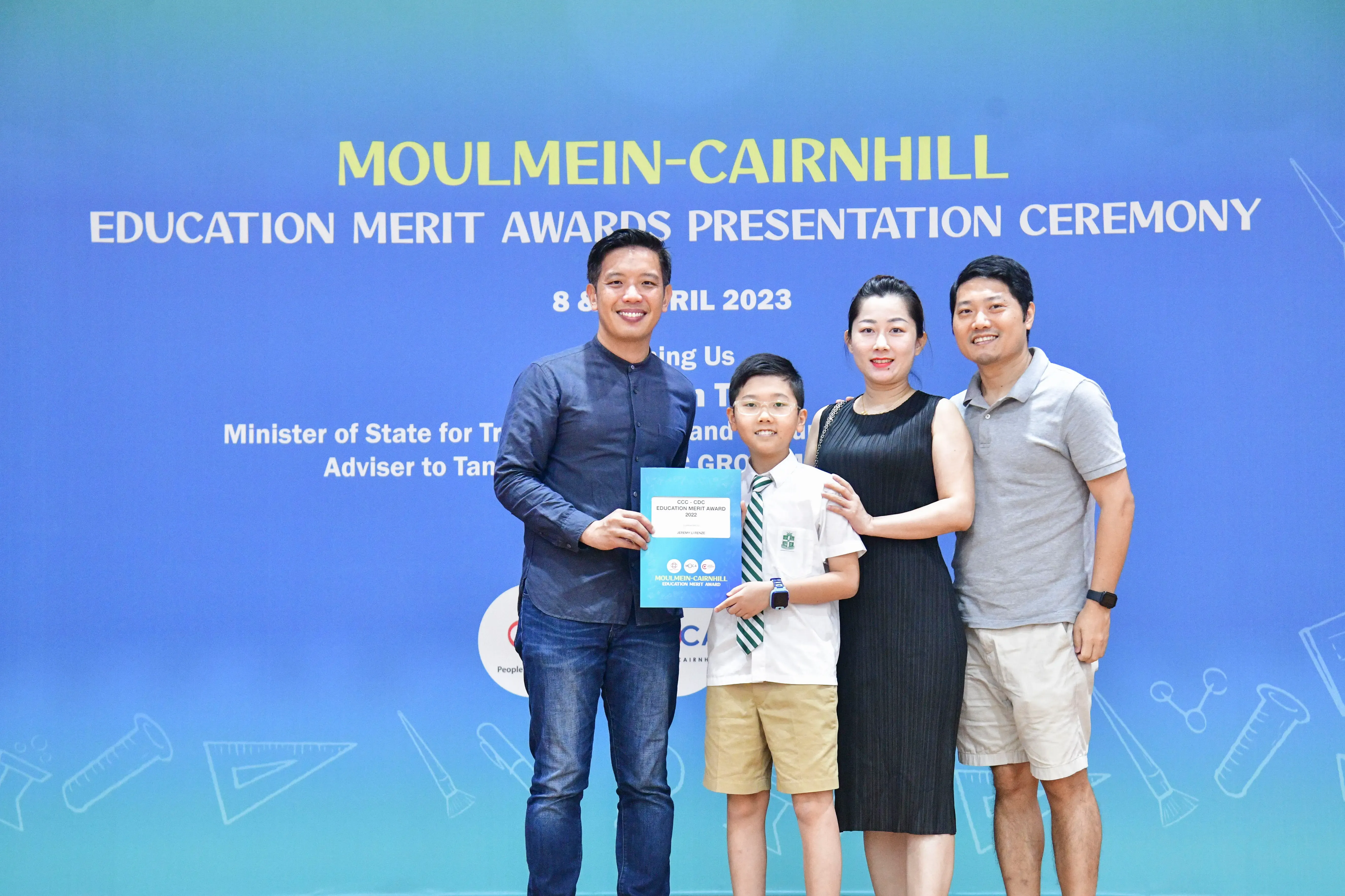 Three adults and a young boy in school uniform hold a certificate at the Moulmein-Cairnhill Education Merit Awards 2023.