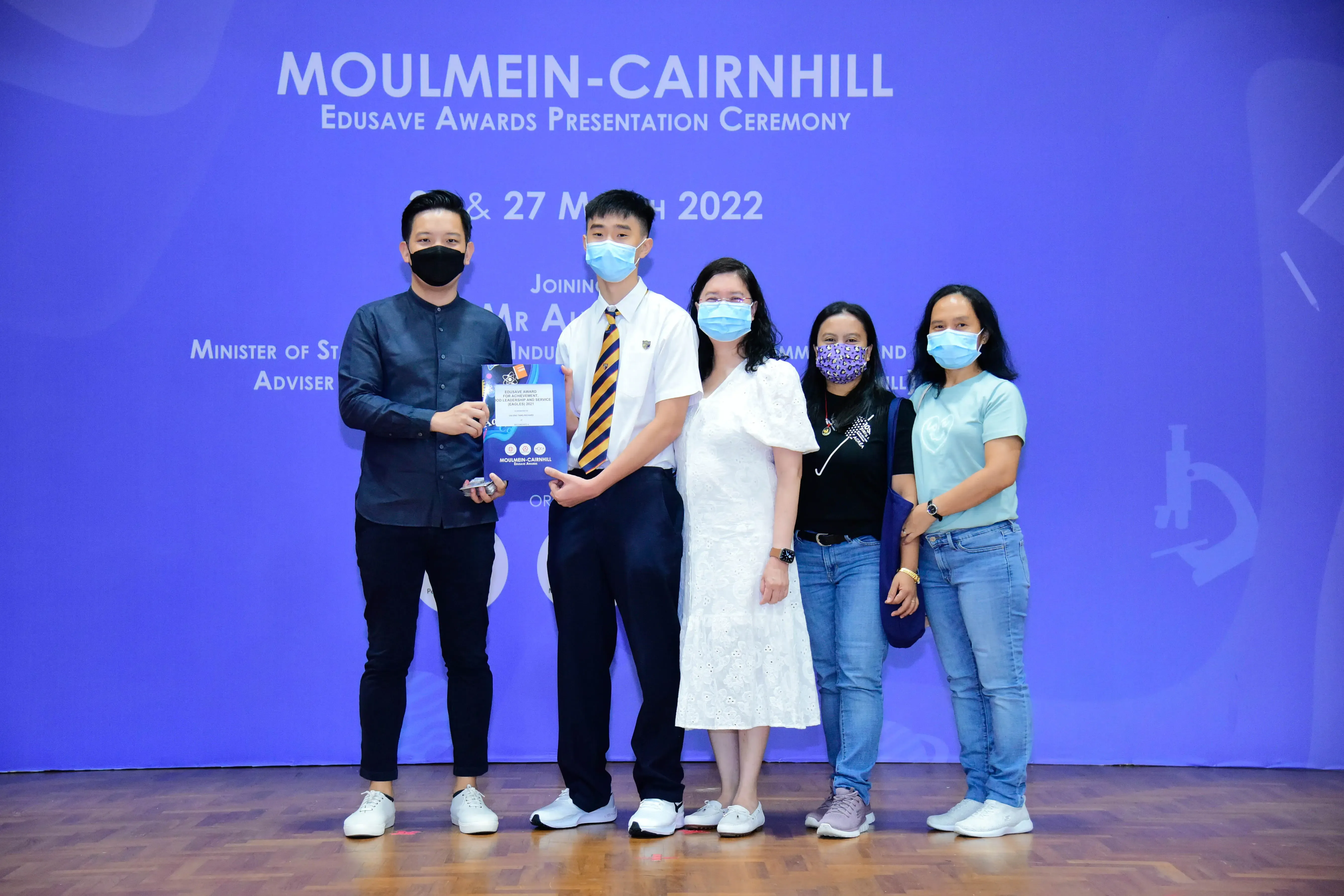 Five masked people pose at the Moulmein-Cairnhill Edusave Awards Presentation Ceremony, holding an award plaque.