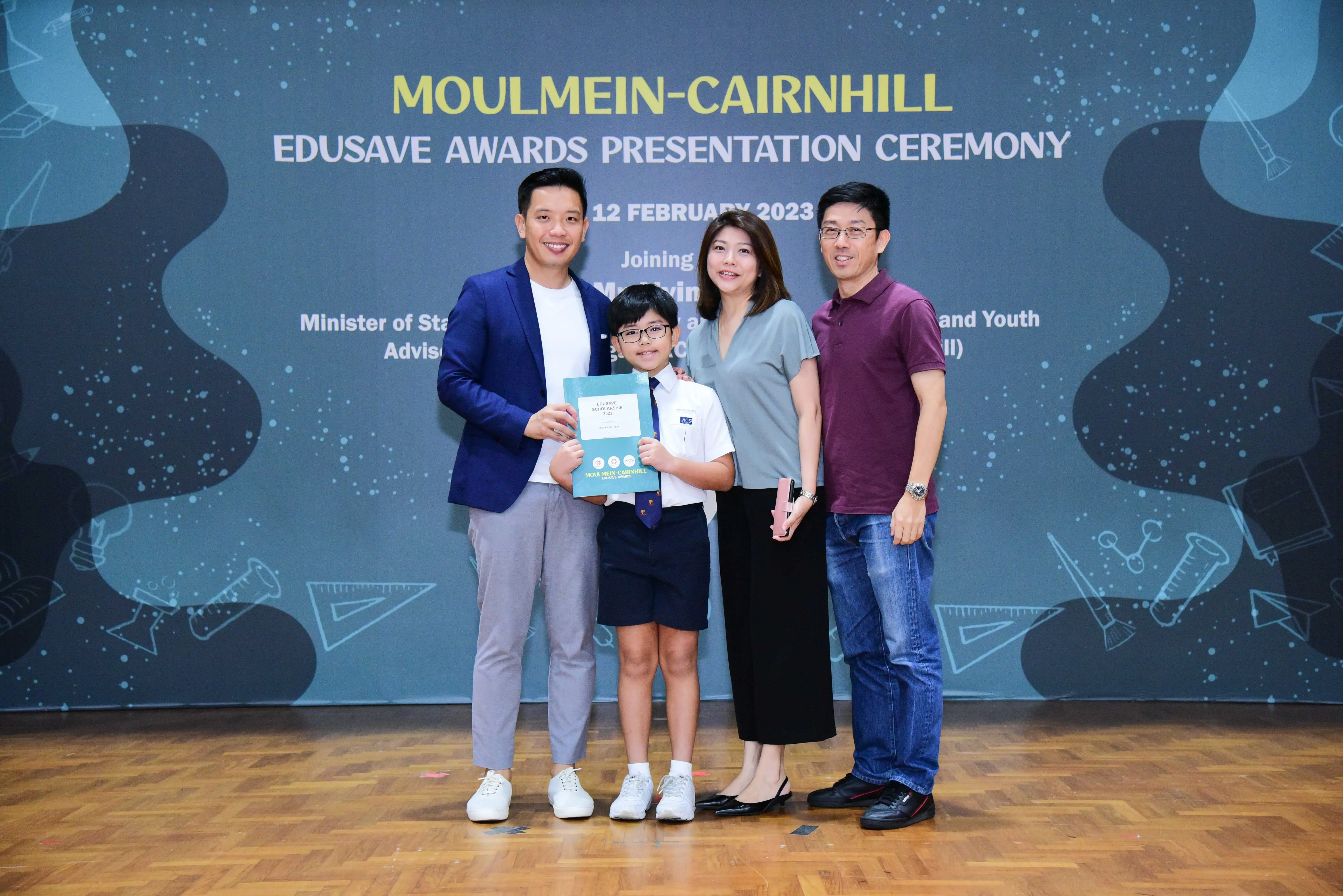 Four people pose at the Moulmein-Cairnhill Edusave Awards Ceremony on 12 February 2023, with a boy holding a certificate.