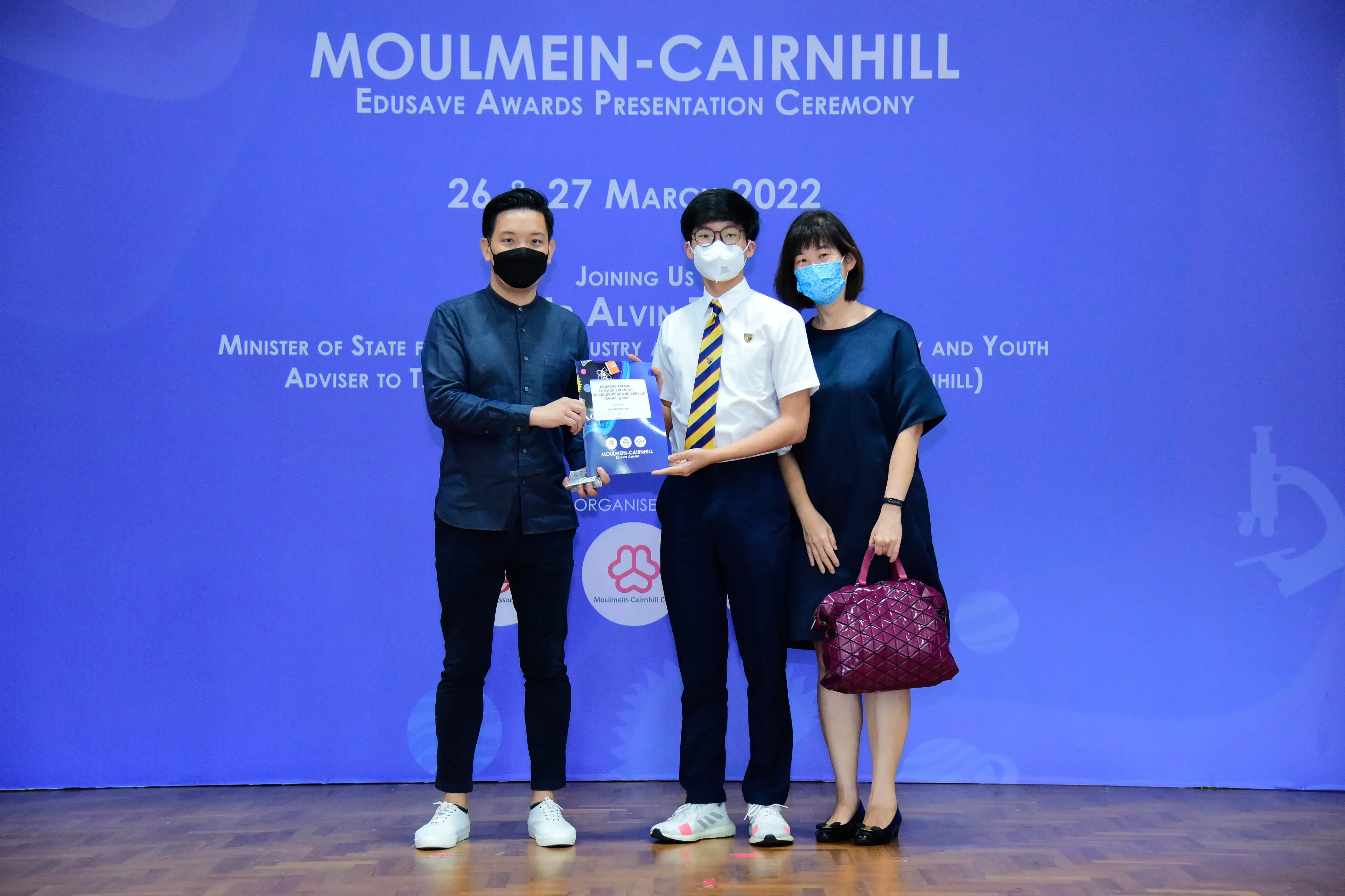 Three masked people pose holding an award at the Moulmein-Cairnhill Edusave Awards Ceremony, March 2022.