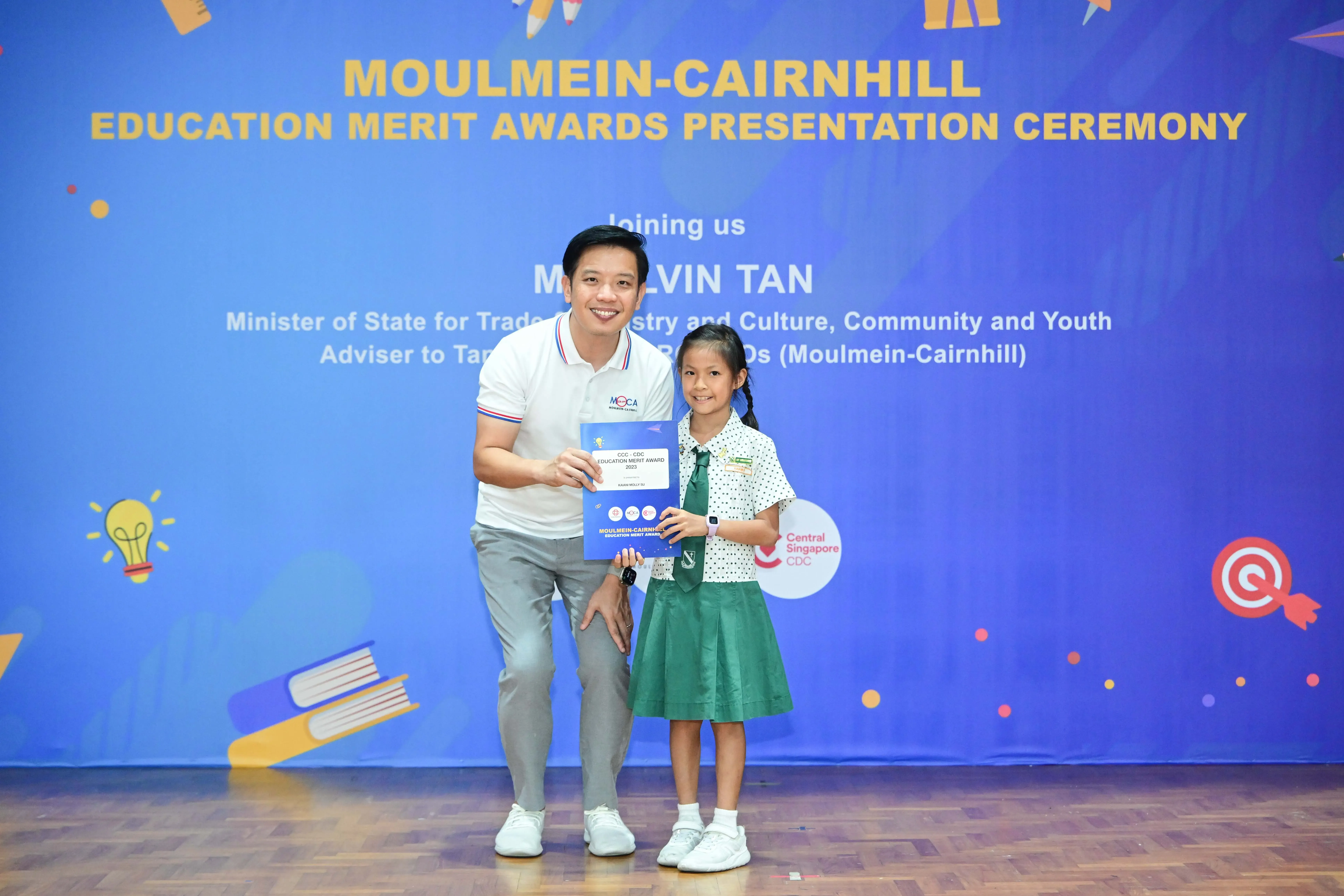A man and a young girl in school uniform hold an award certificate at the Moulmein-Cairnhill Education Merit Awards ceremony.