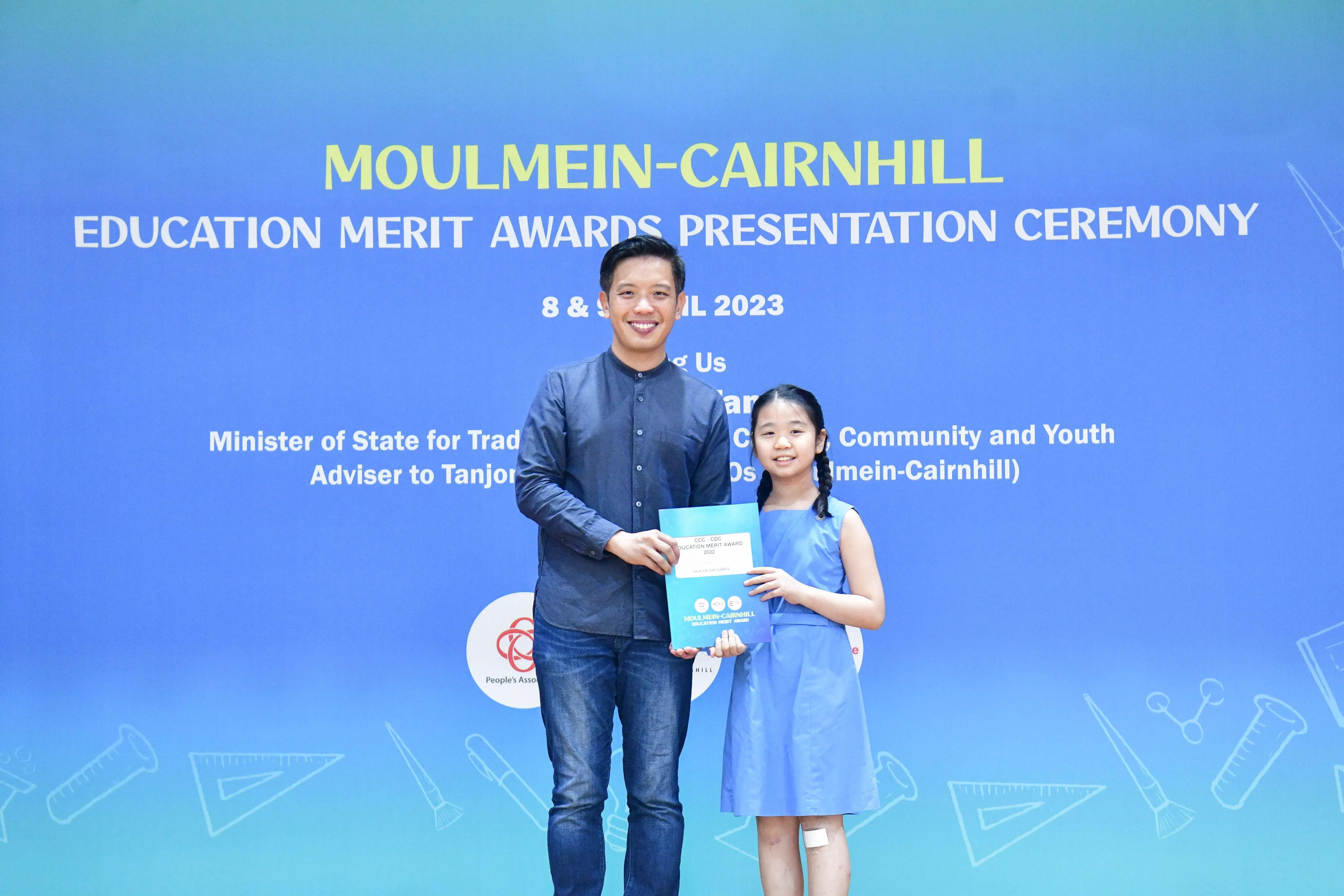 A man and a young girl hold an award certificate at the Moulmein-Cairnhill Education Merit Awards Ceremony 2023.