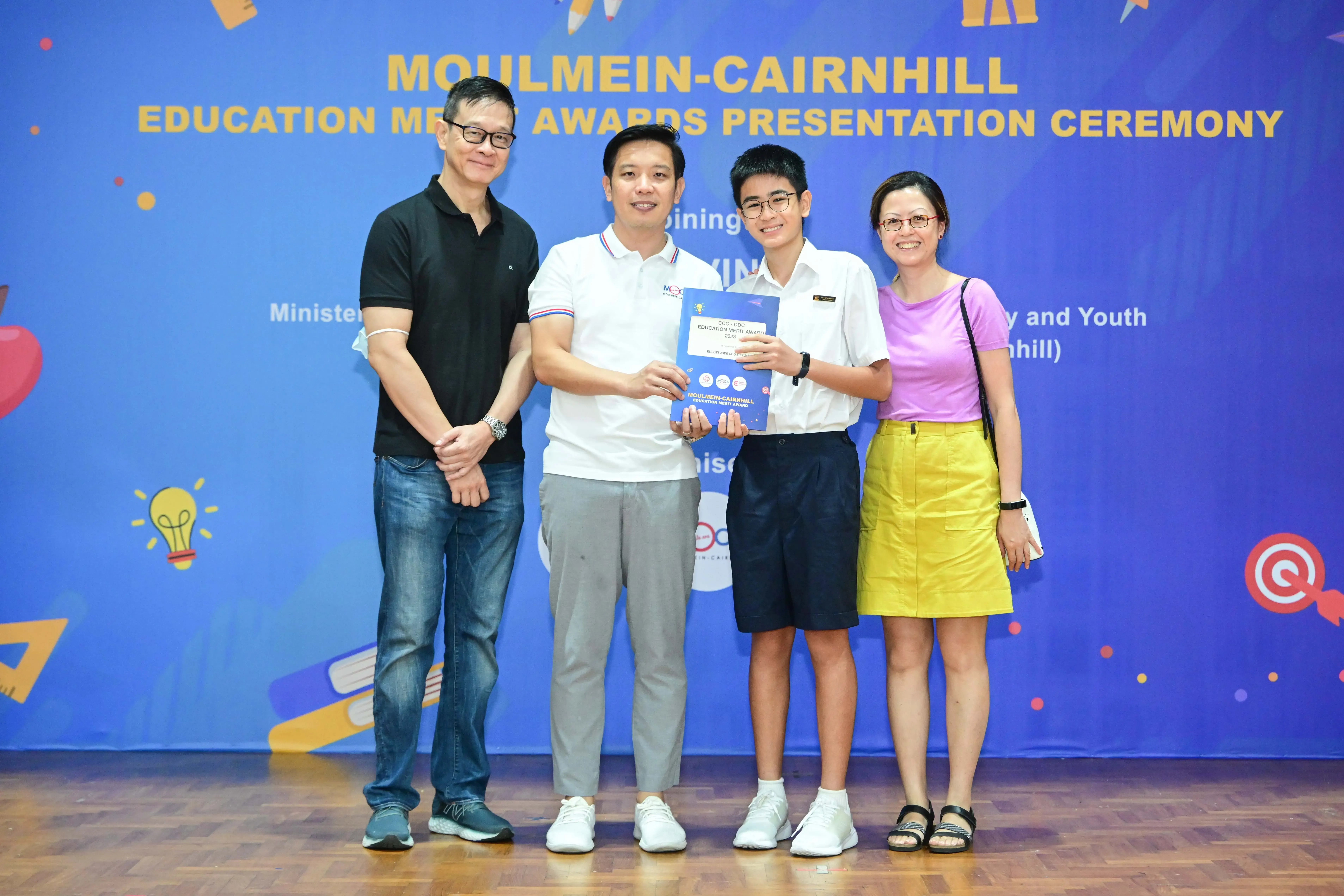 Four people pose together at the Moulmein-Cairnhill Education Merit Awards Presentation Ceremony, holding a certificate.