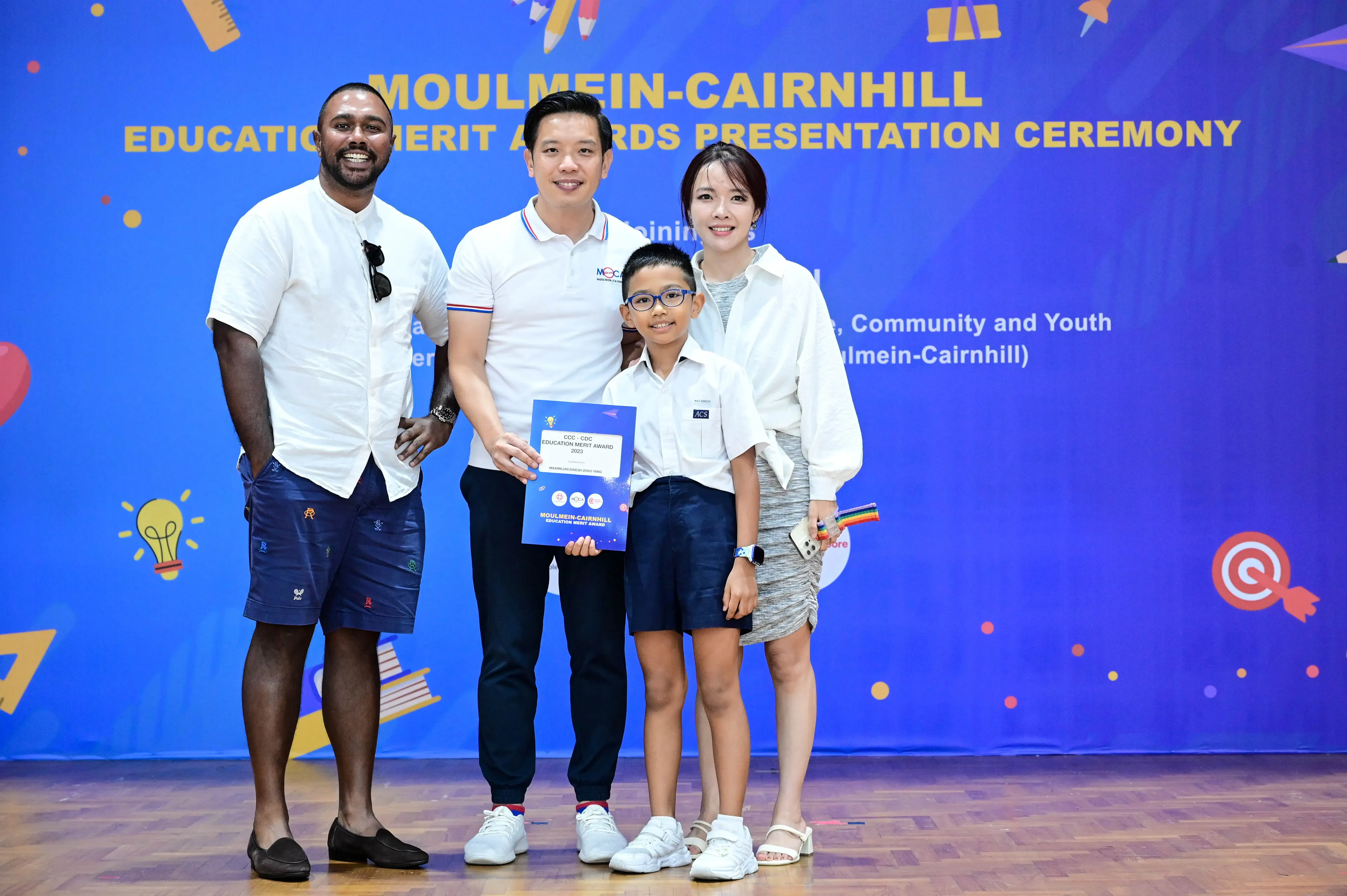 Three adults and a boy holding an award certificate pose at the Moulmein-Cairnhill Education Merit Awards ceremony.