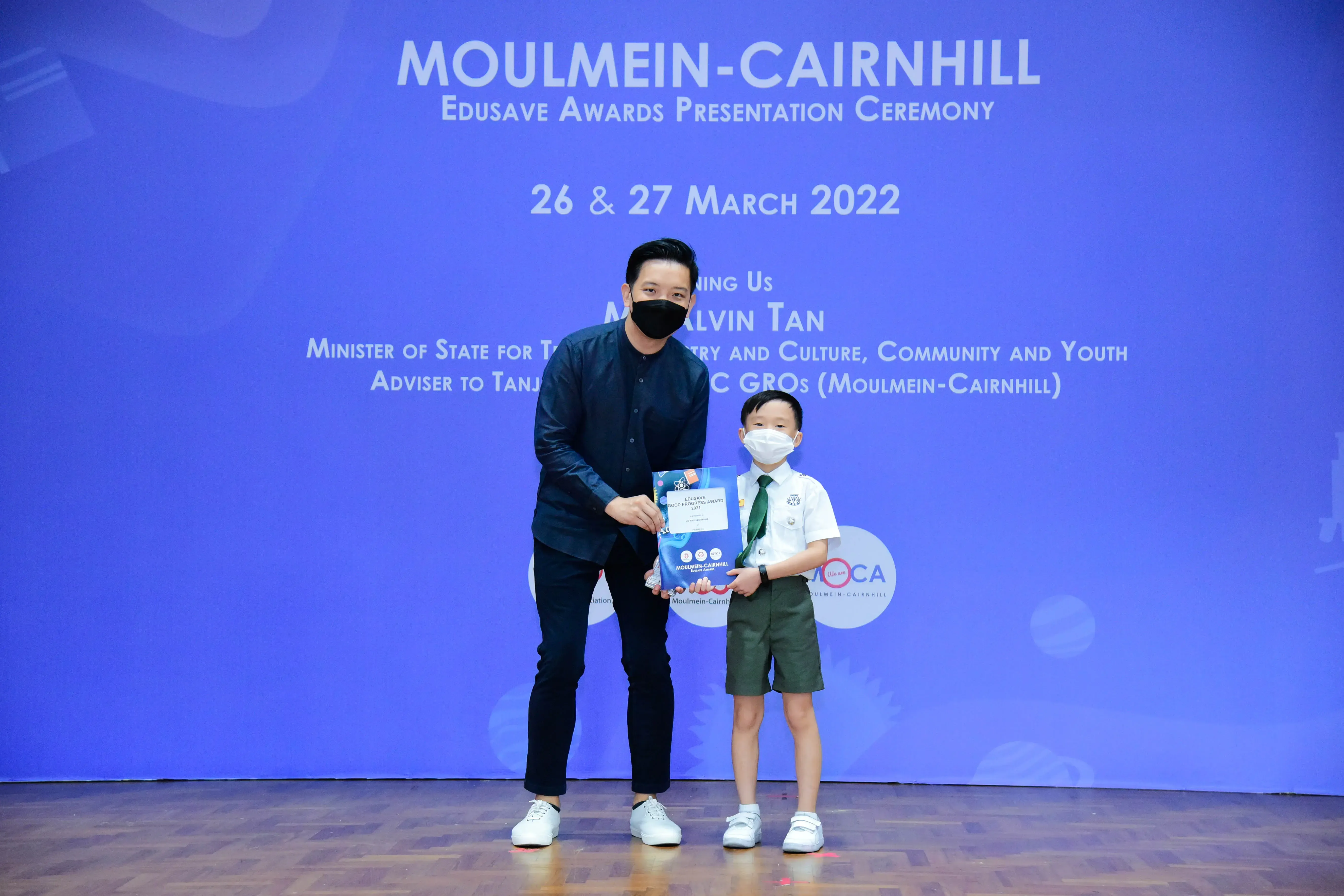 An adult and a young student in uniform hold an award together at the Moulmein-Cairnhill Edusave Awards Ceremony 2022.