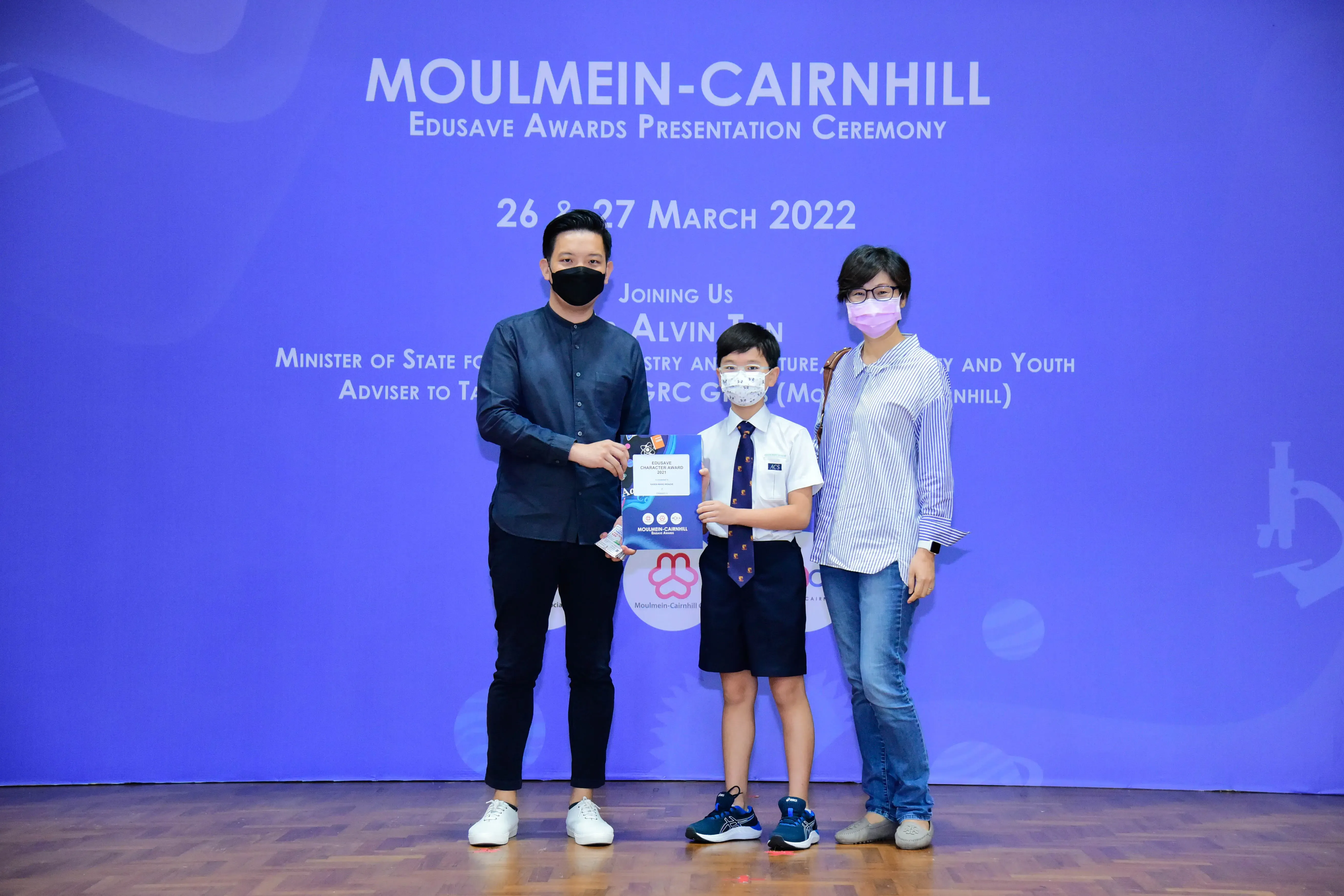 Three masked people pose with an award certificate at the Moulmein-Cairnhill Edusave Awards Ceremony, March 2022.