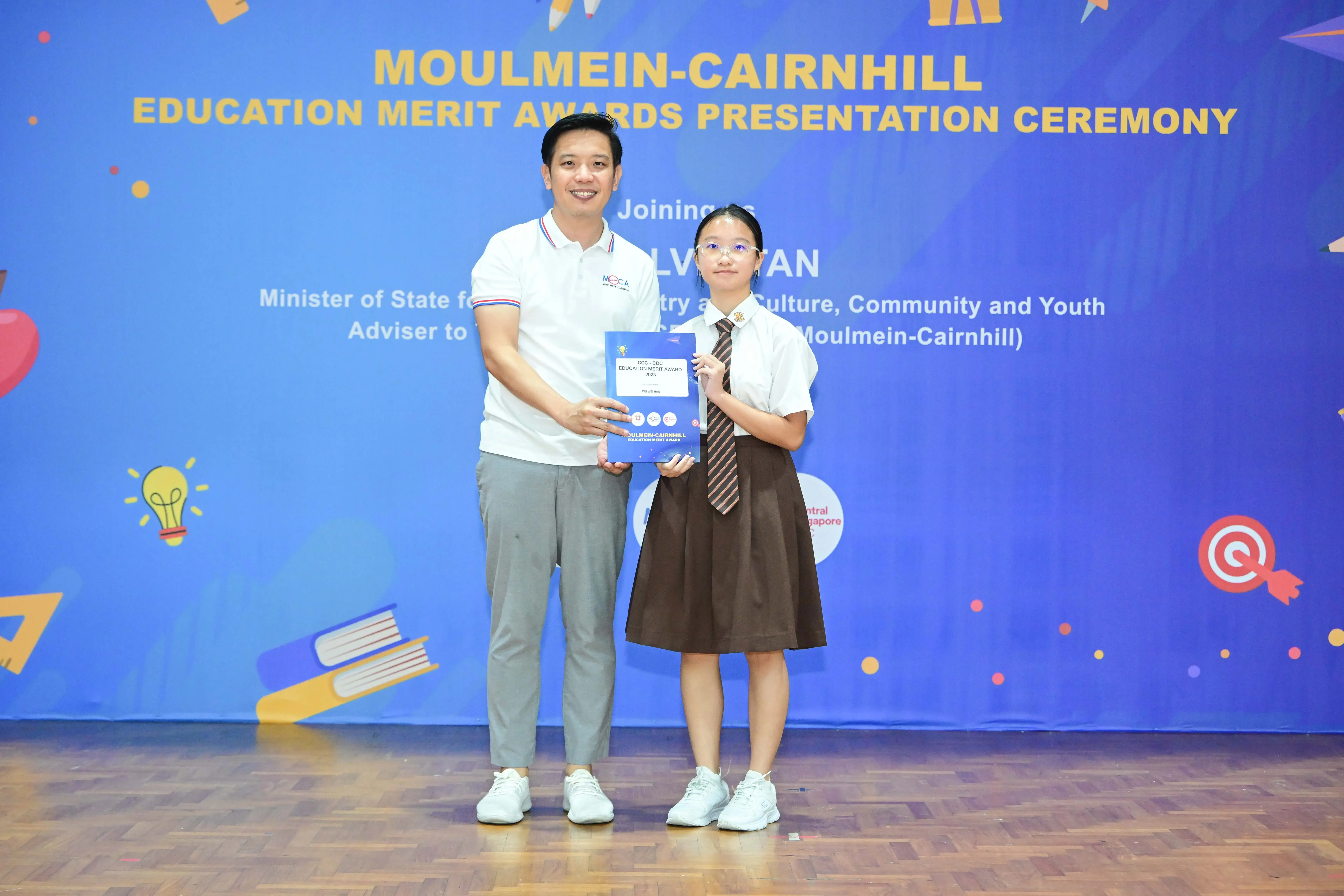 A man and a uniformed schoolgirl hold a certificate together at the Moulmein-Cairnhill Education Merit Awards Ceremony.