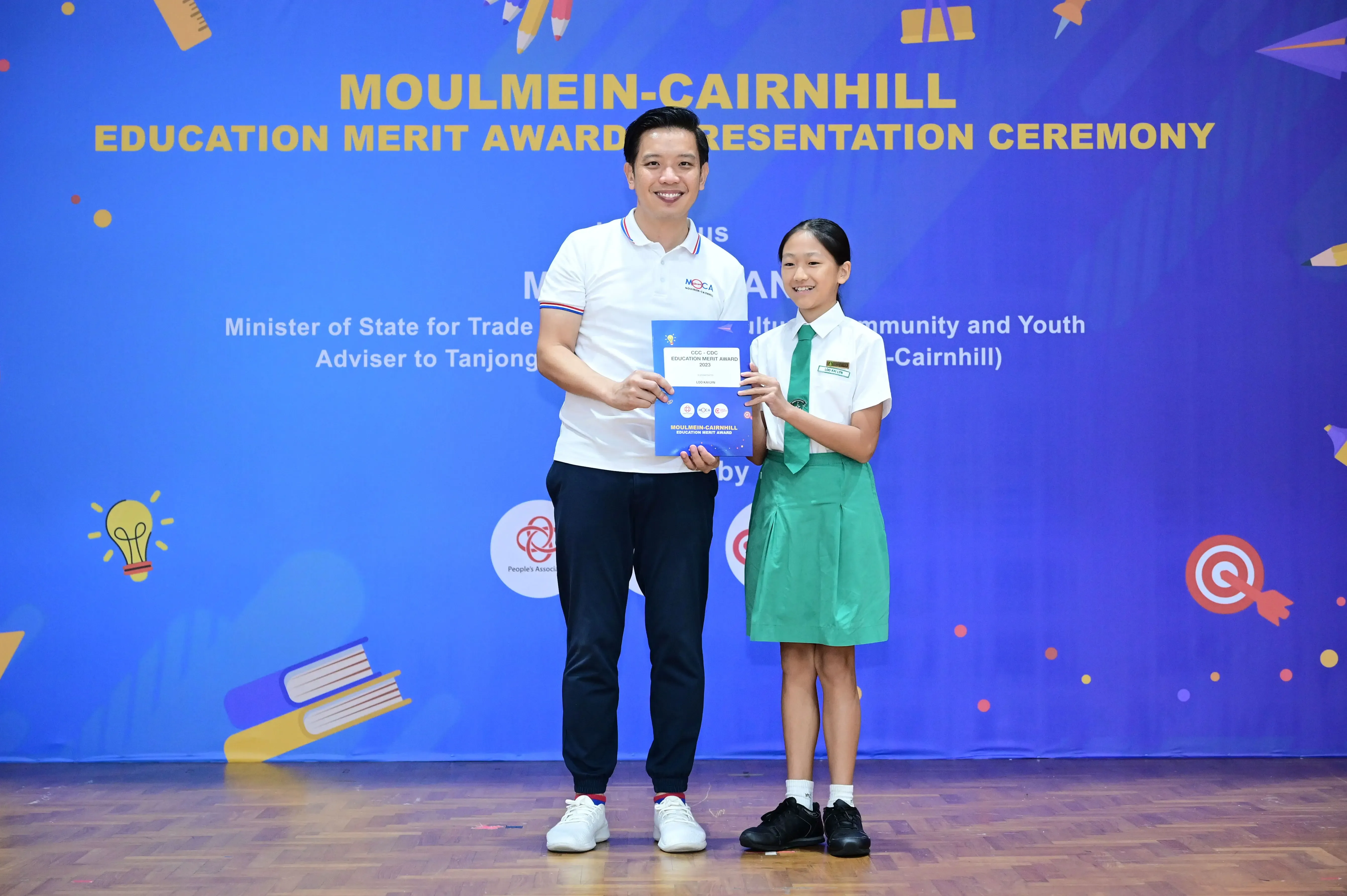 A man and a young girl in school uniform hold an award certificate at the Moulmein-Cairnhill Education Merit Award Ceremony.
