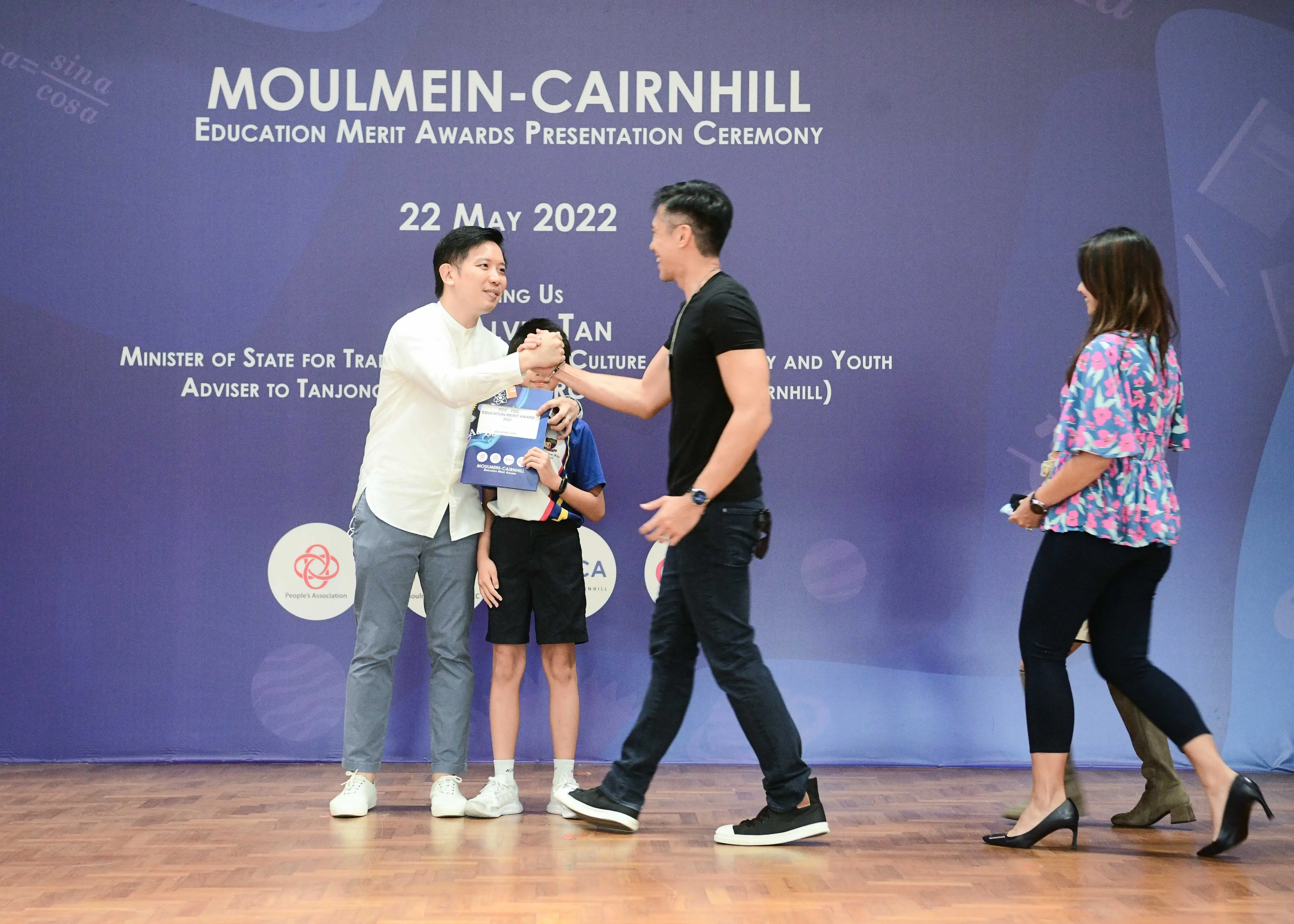 Two men shake hands on stage at the Moulmein-Cairnhill Education Merit Awards on 22 May 2022.