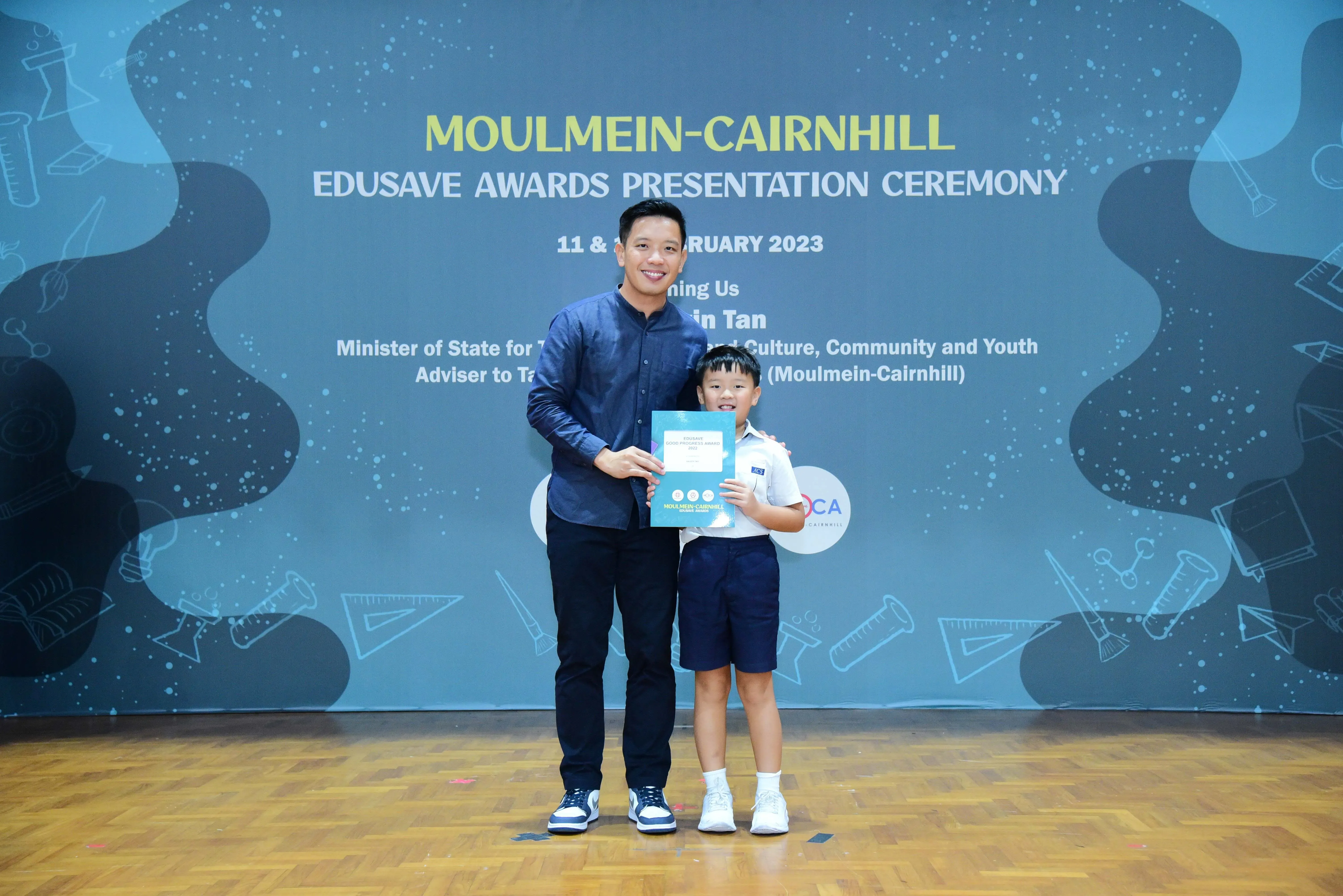 An adult and a young boy hold a certificate at the Moulmein-Cairnhill Edusave Awards Presentation Ceremony 2023.