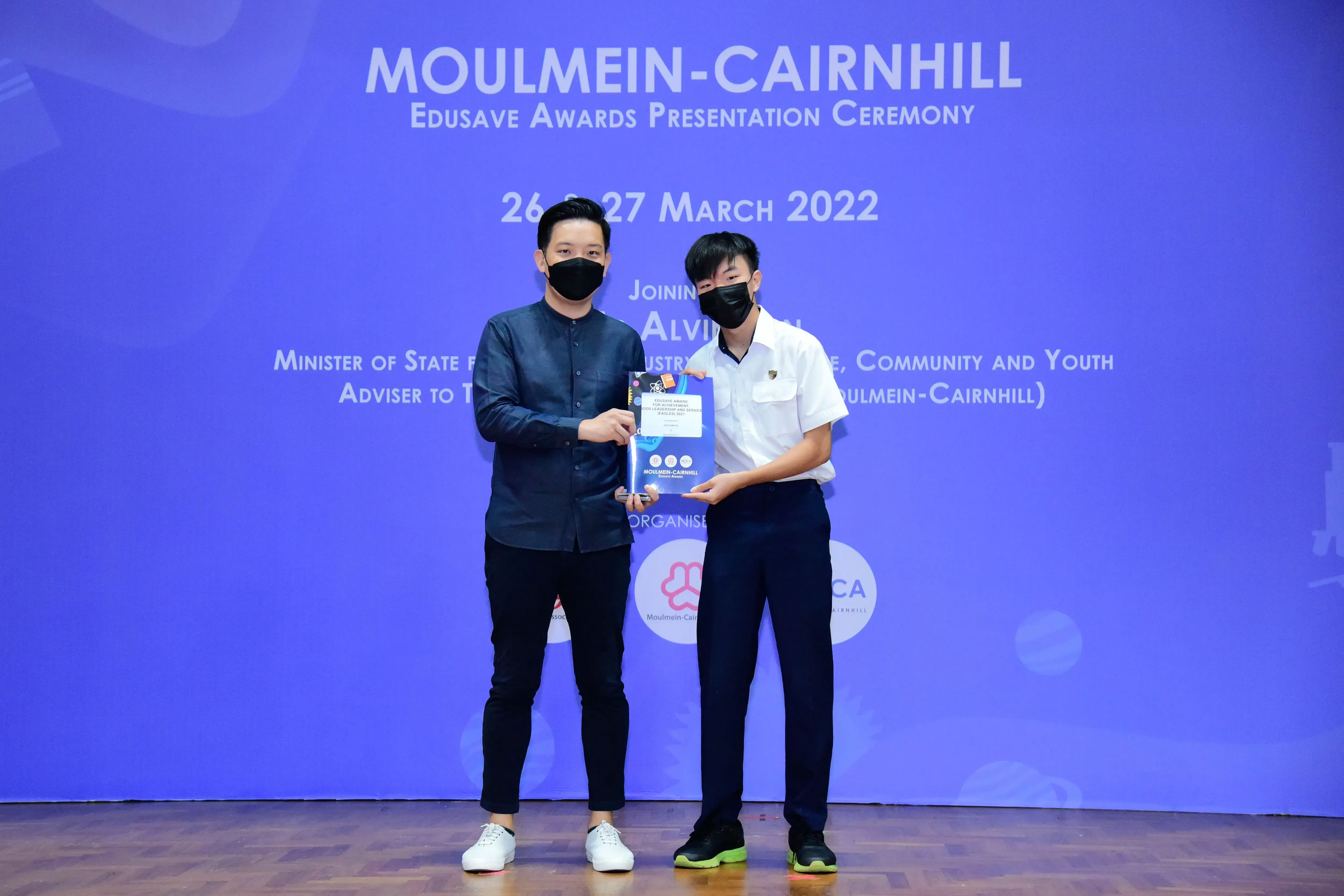 Two masked men hold a certificate at the Moulmein-Cairnhill Edusave Awards Ceremony, March 2022.