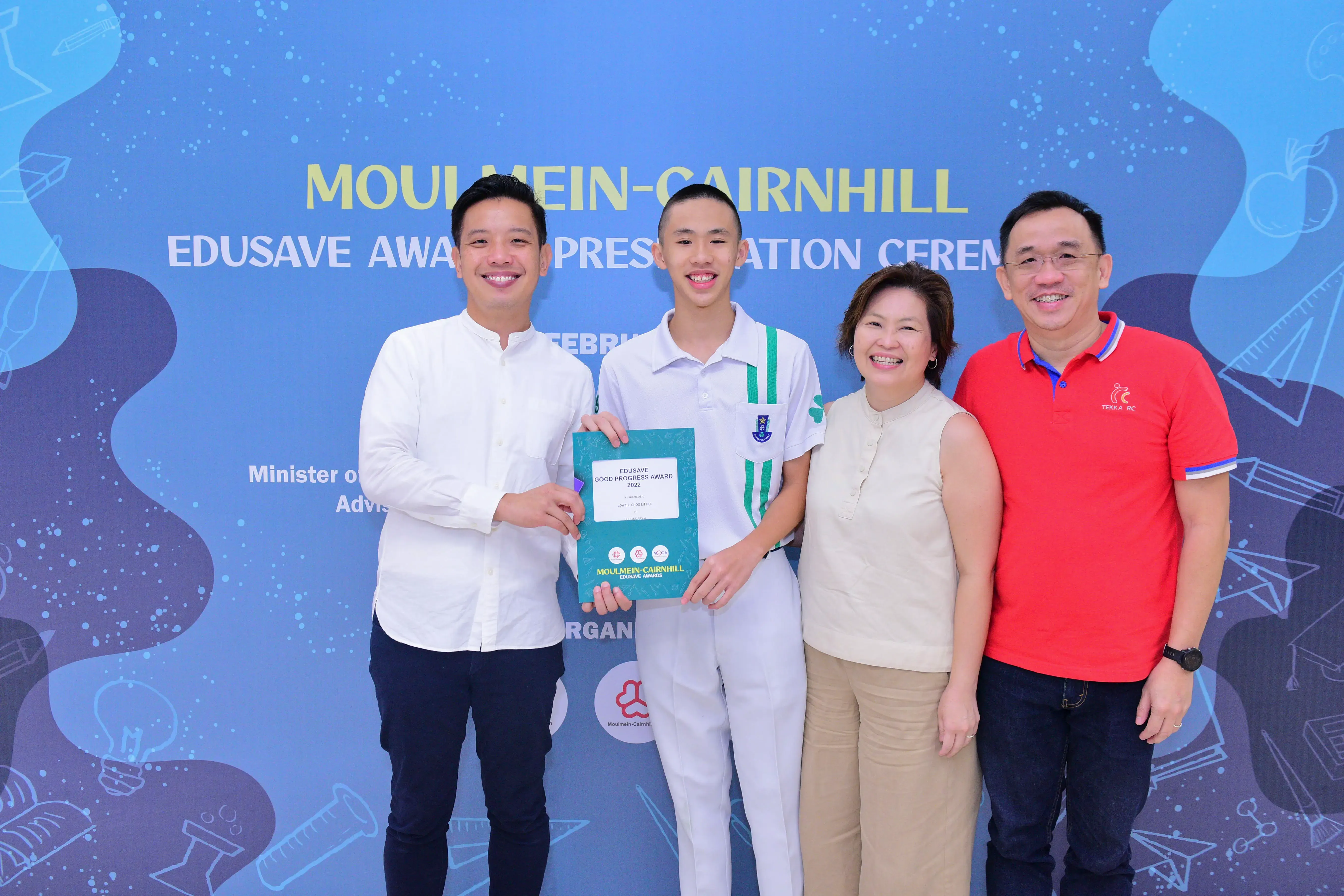 Four people smiling at the Moulmein-Cairnhill Edusave Award ceremony, with a student holding a certificate.