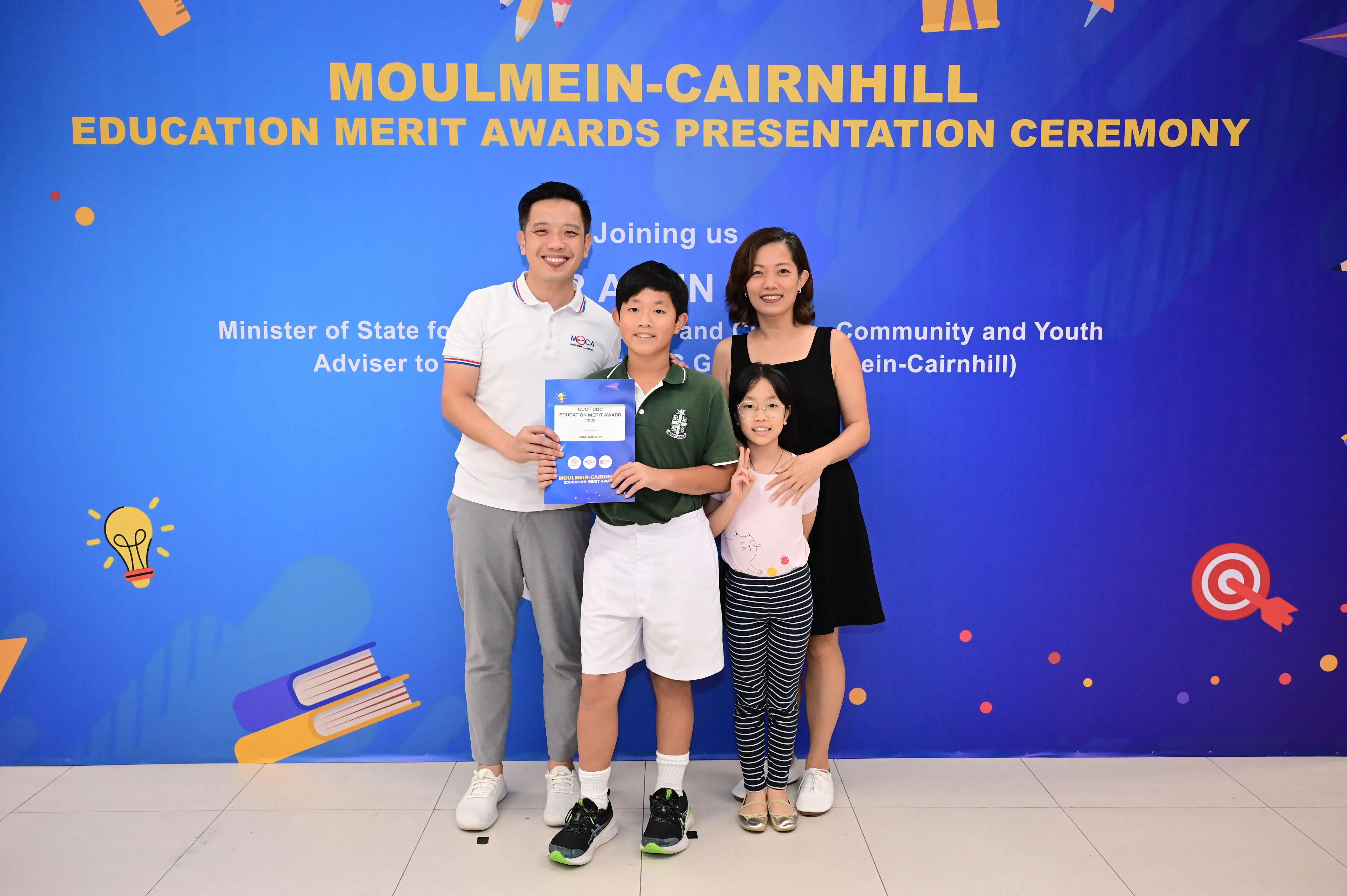 Family of four posing with an award certificate at the Moulmein-Cairnhill Education Merit Awards ceremony.