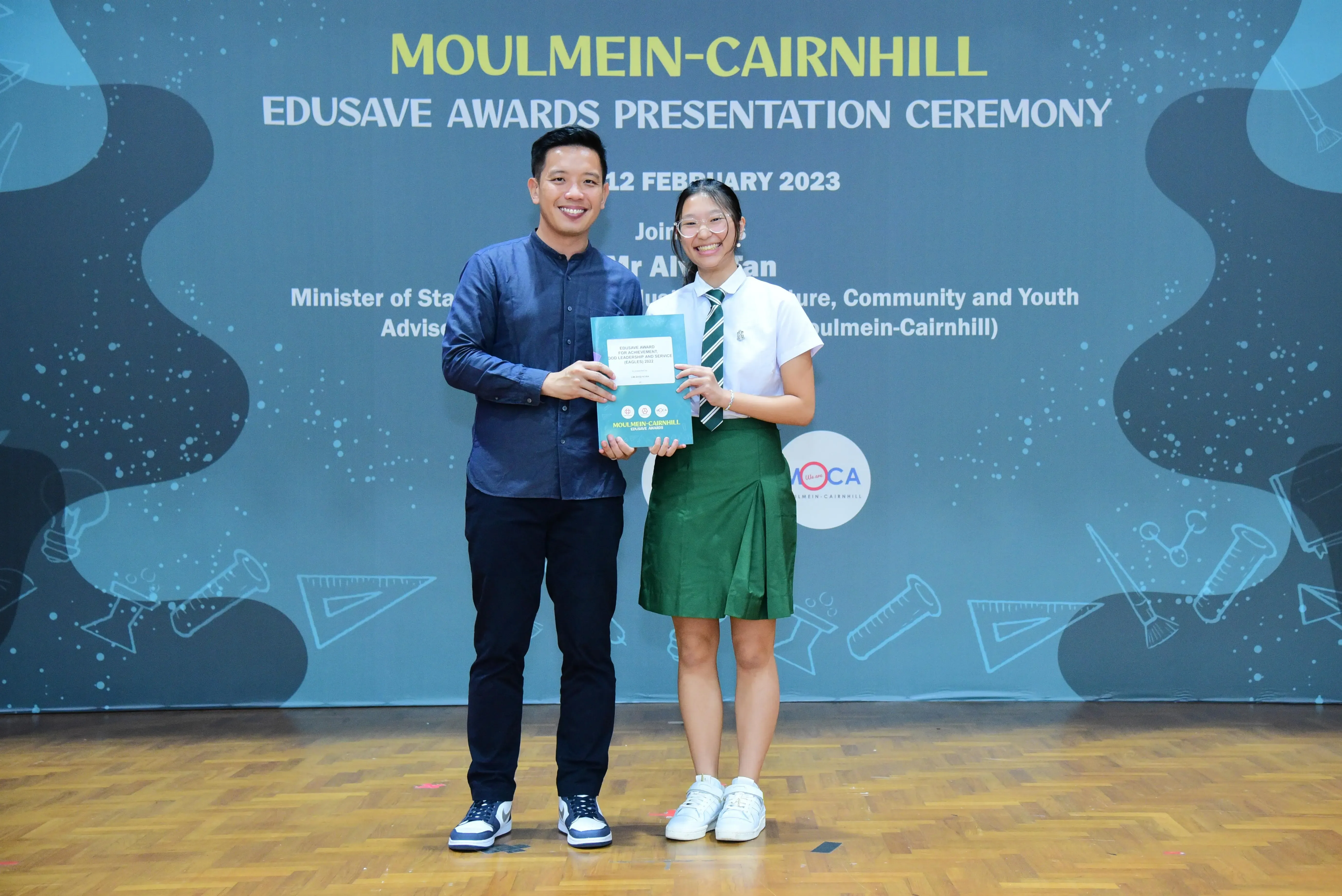 Two people smile while holding an award booklet at the Moulmein-Cairnhill Edusave Awards Ceremony on 12 February 2023.