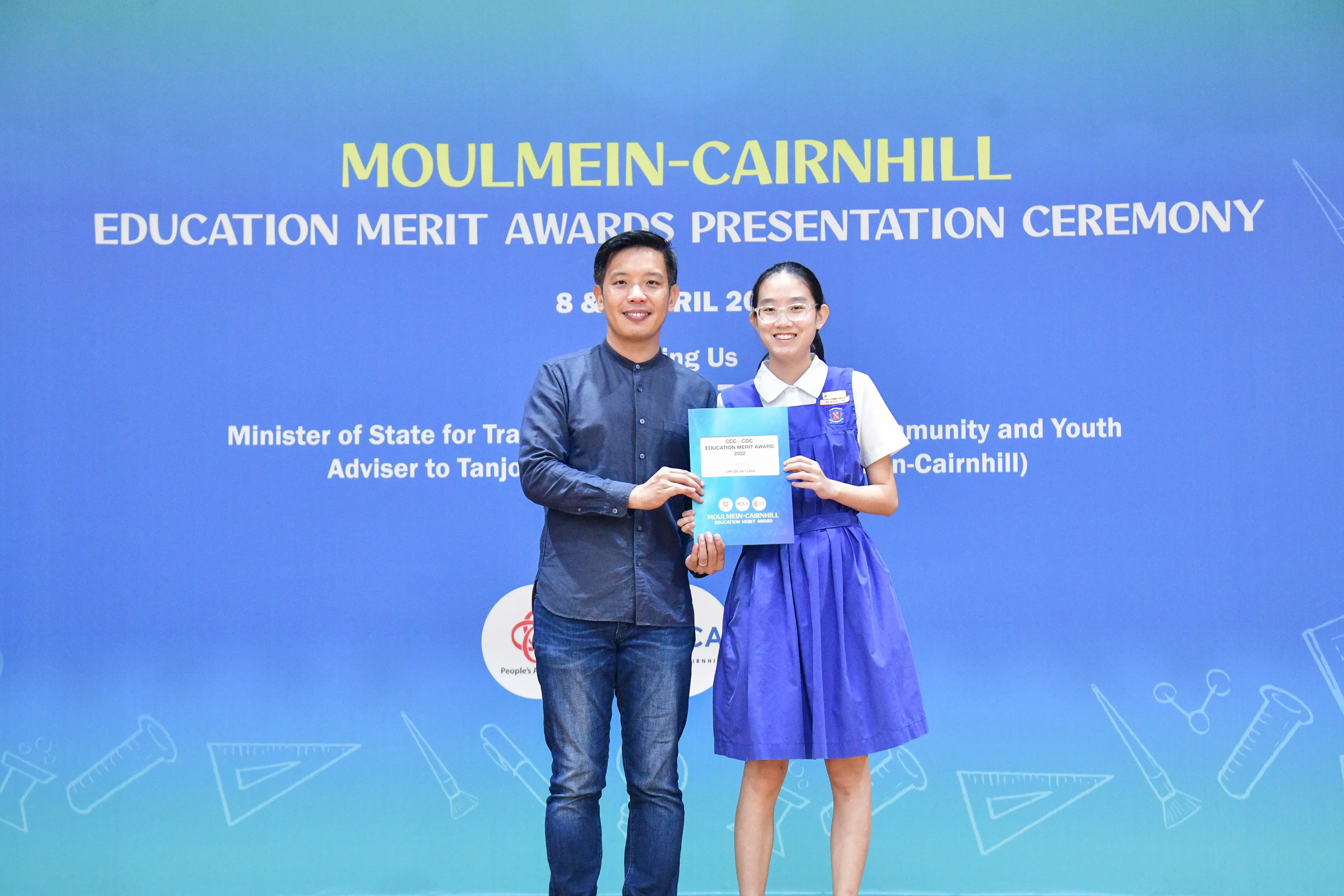 A man and a young girl in school uniform hold a certificate at the Moulmein-Cairnhill Education Merit Awards ceremony.